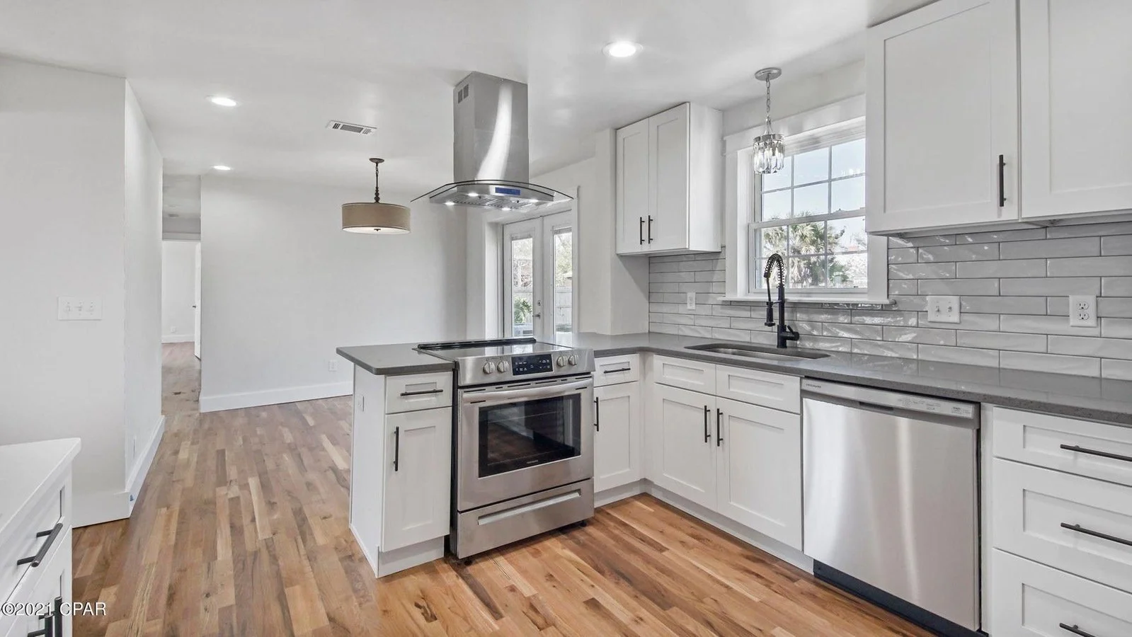 Modern kitchen with white cabinets, gray countertops, stainless steel appliances, hardwood floors, and a large window.
