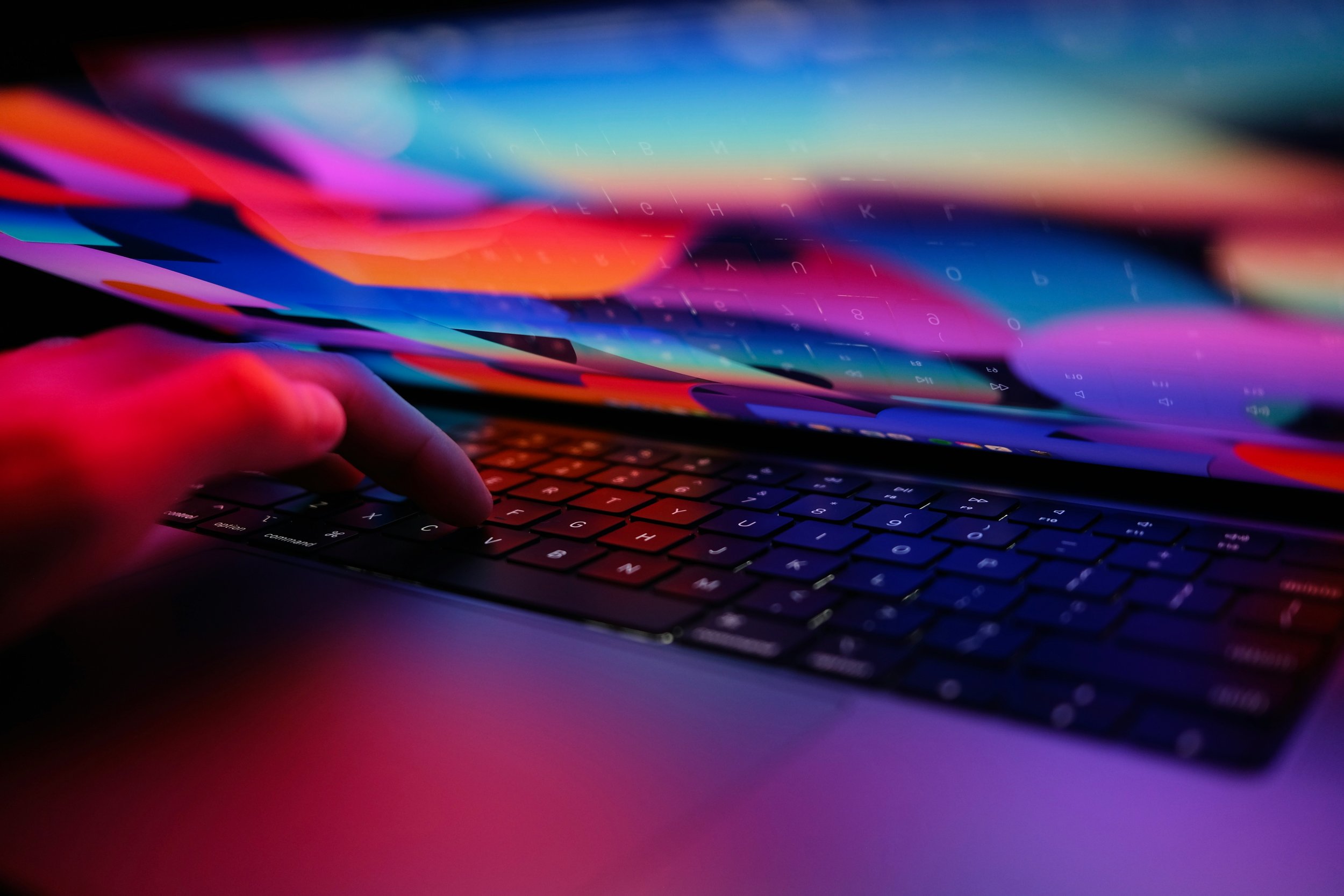 Une main tapant sur le clavier d'un ordinateur portable, avec un écran affichant des couleurs vives et une interface numérique.