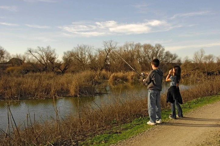 Two children, a boy and a girl, fishing by a river during daytime.