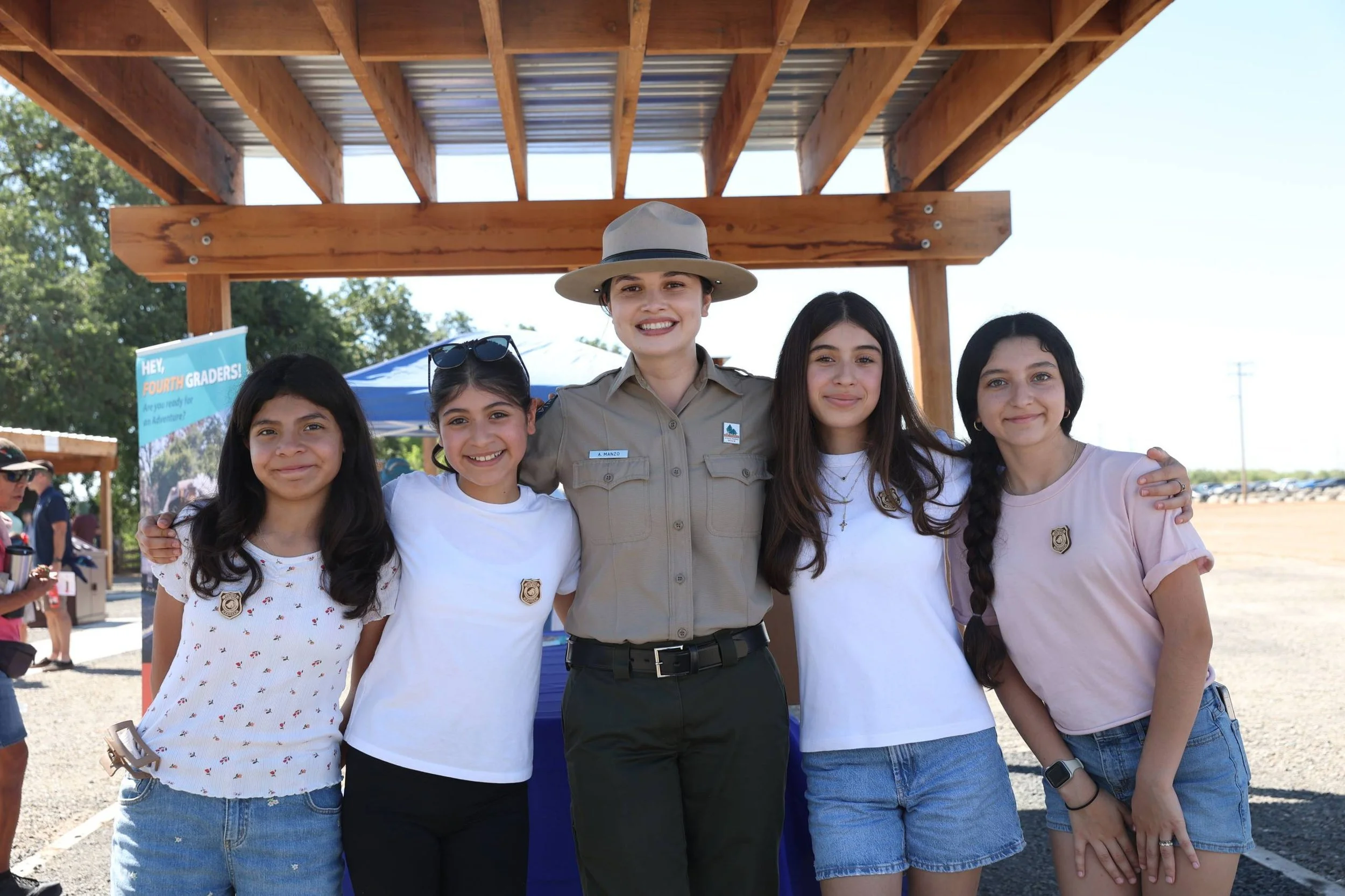 A woman in a park ranger uniform standing with four young girls, all smiling for the photo.