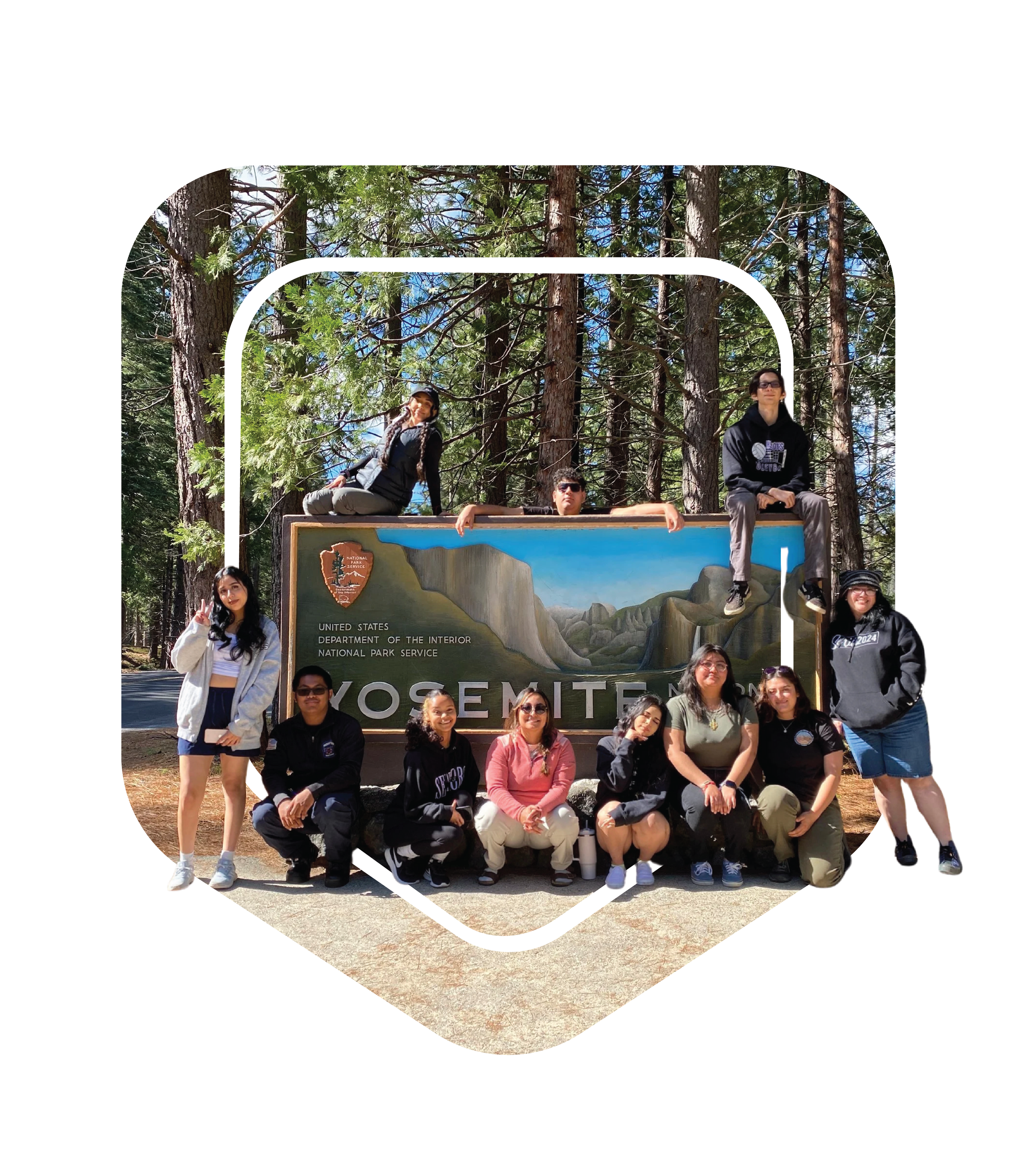 Group of people posing in front of a Yosemite National Park sign surrounded by tall trees.