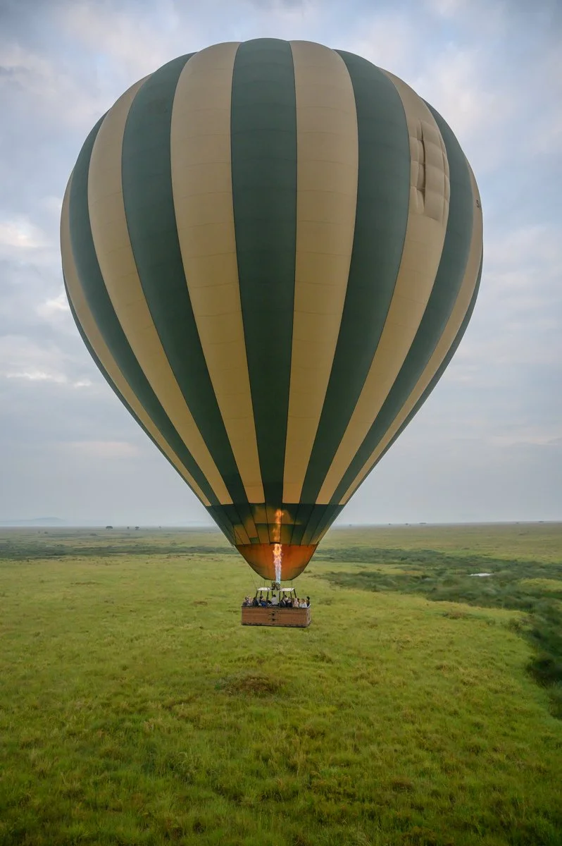 A hot air balloon flying over a grassy landscape with a burner flame at the base of the balloon.