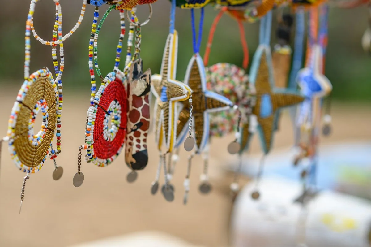 Colorful beaded and fabric pouches and jewelry hanging on display, with star-shaped ornaments and small metallic tags, outdoors on a blurred background.