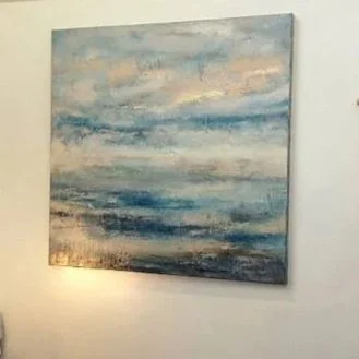 Abstract painting with shades of blue, beige, and white, hanging on a white wall.