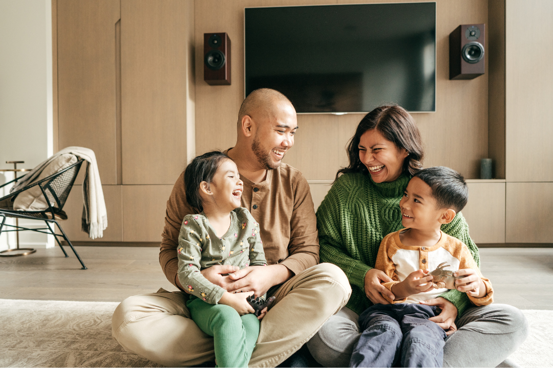 A family of four sitting on the floor in their living room, excited and laughing together.