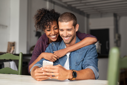 A happy couple looking at a smartphone together in a cozy home setting.