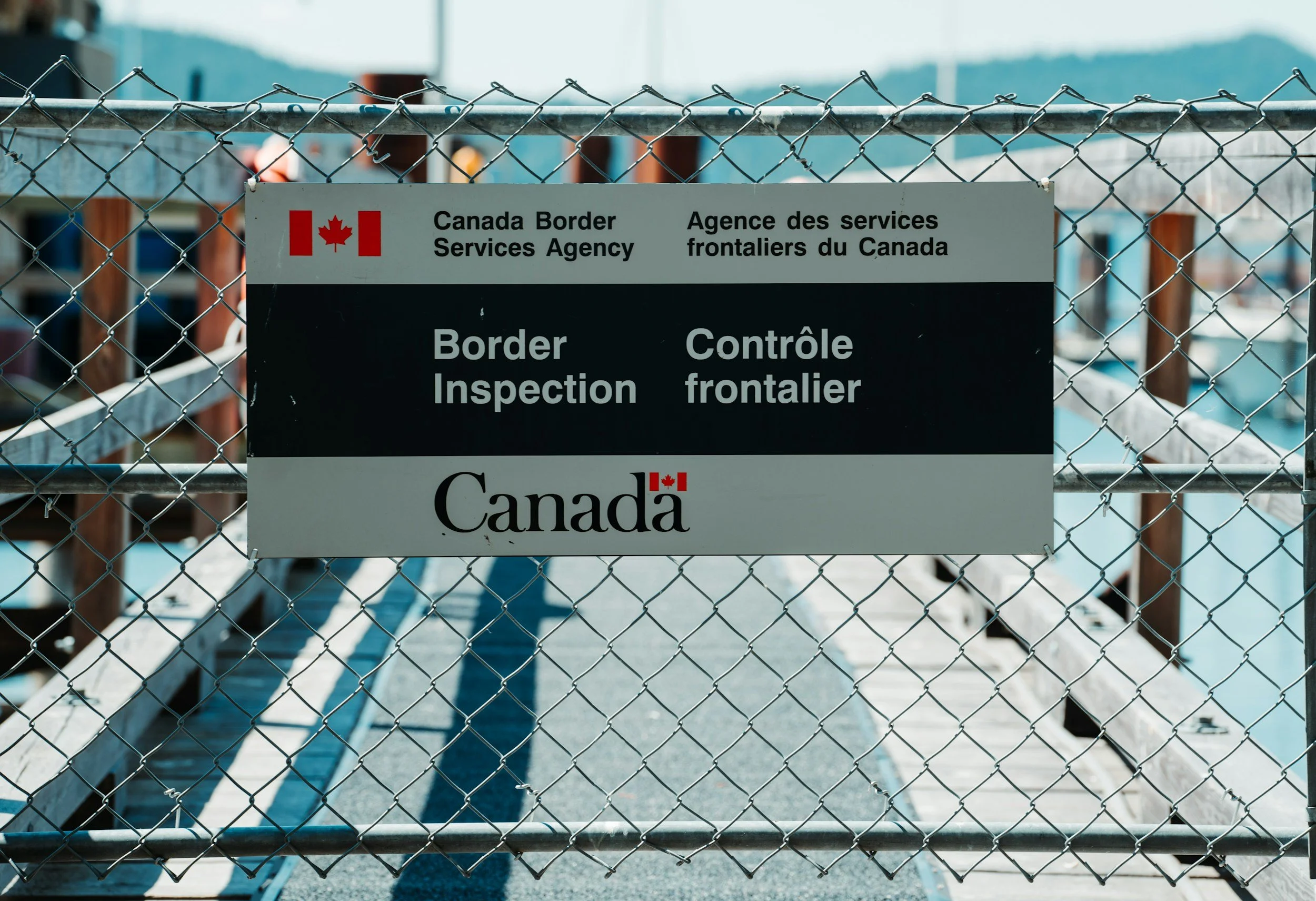 Fenced border inspection station at the Canadian border with a sign reading 'Canada Border Services Agency Border Inspection,' with the Canadian flag and bilingual text.