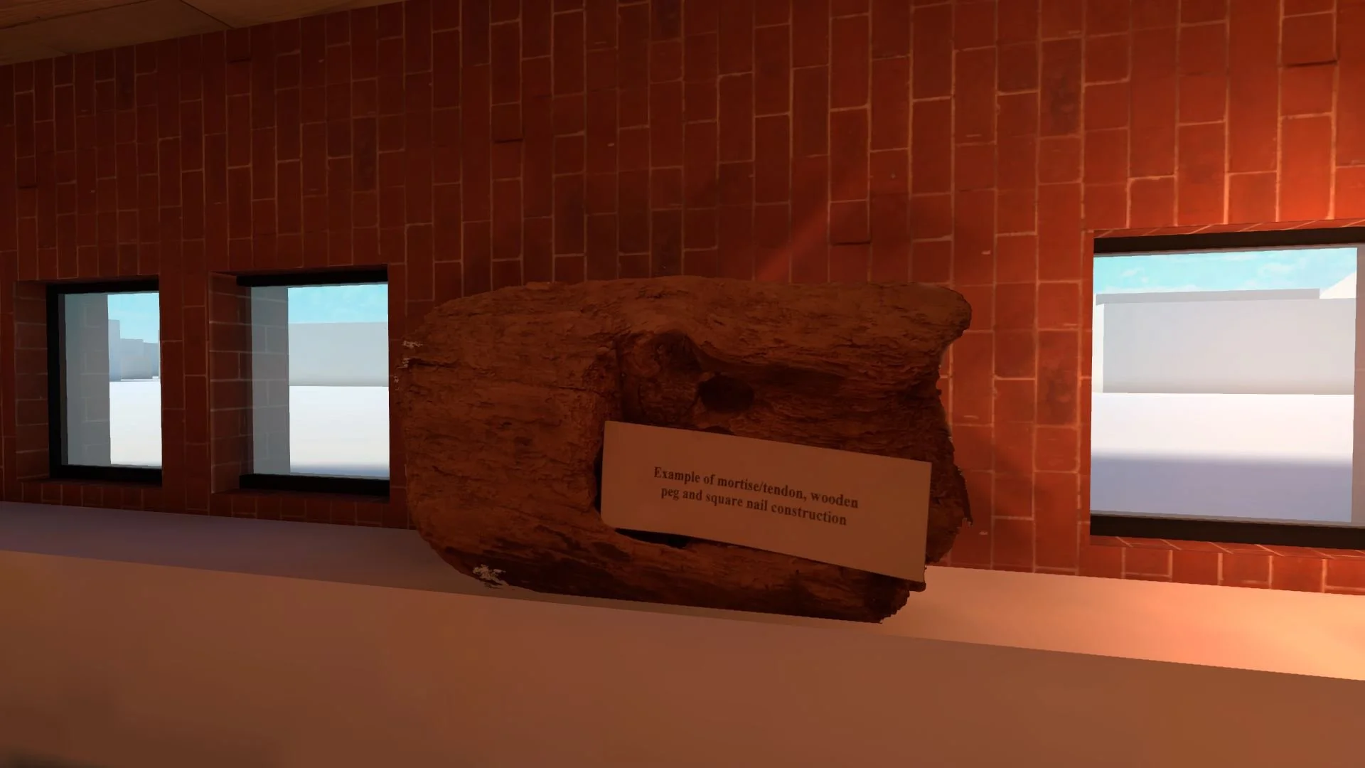 A display of a large piece of wood on a stand with a sign that reads "Example of mortise/tendon, wooden peg and square nail construction". Behind the wood are three small windows on a brick wall.