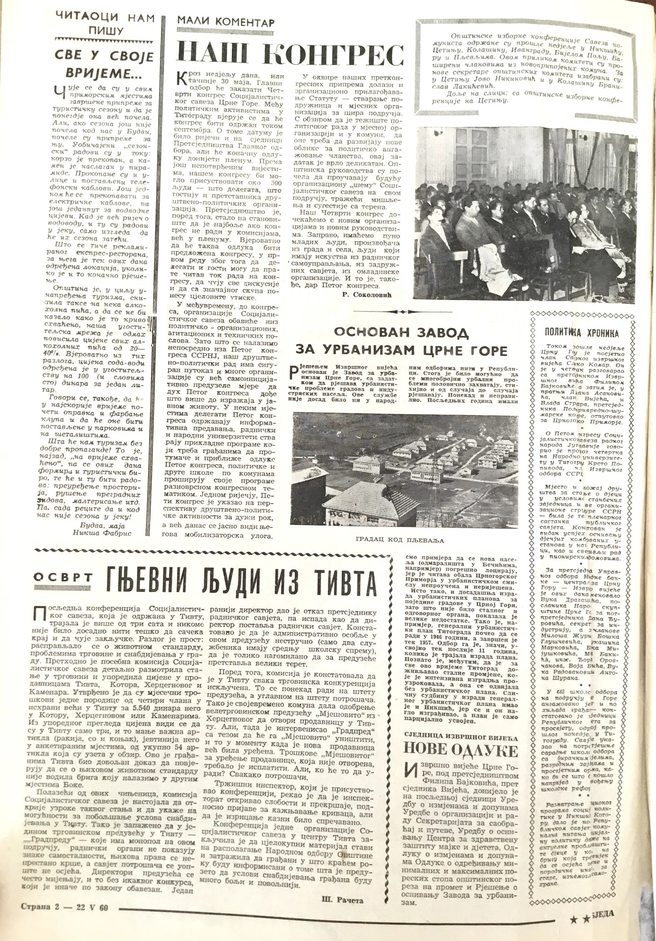 Black and white photograph of a conference room filled with attendees seated at desks. A speaker stands at a podium in front of a presentation screen.