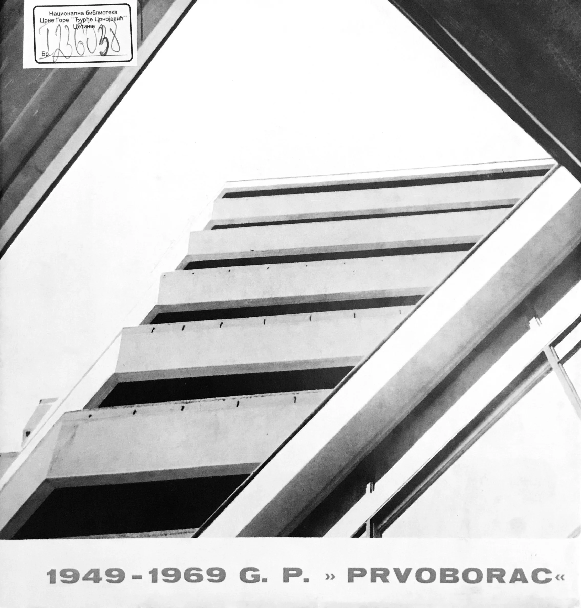 Black and white photo of a tall, multi-story building with balconies, viewed from below. The photo is framed by the edges of the building and part of a balcony railing is visible. There are labels with text in a foreign language and a date range of 1949 to 1969.