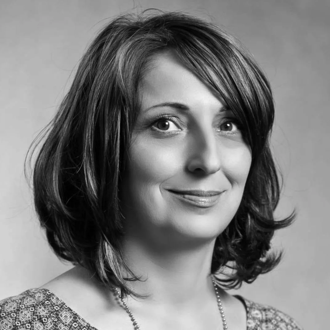 Black and white portrait of a smiling woman with shoulder-length hair, wearing a patterned top and a necklace.