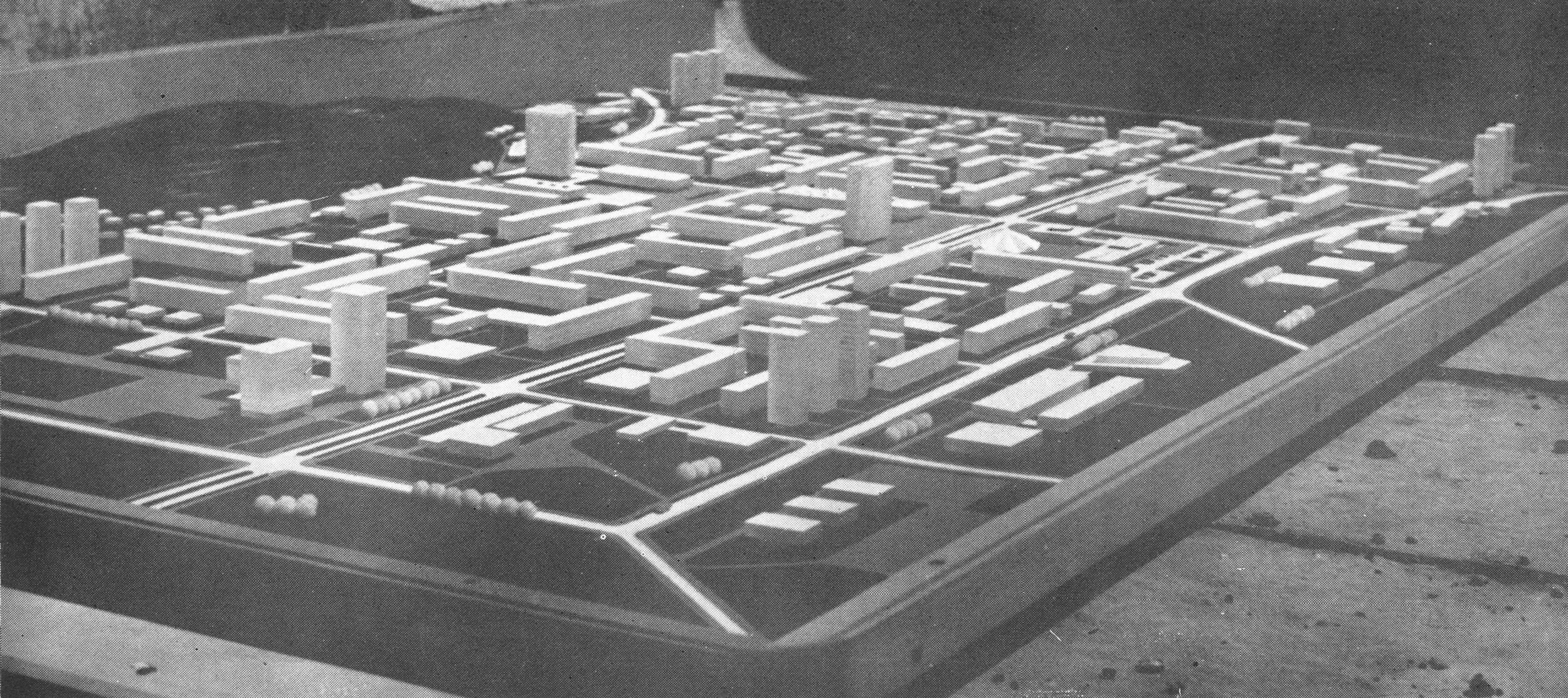 A black and white architectural scale model of a city layout with numerous buildings, roads, and open spaces.