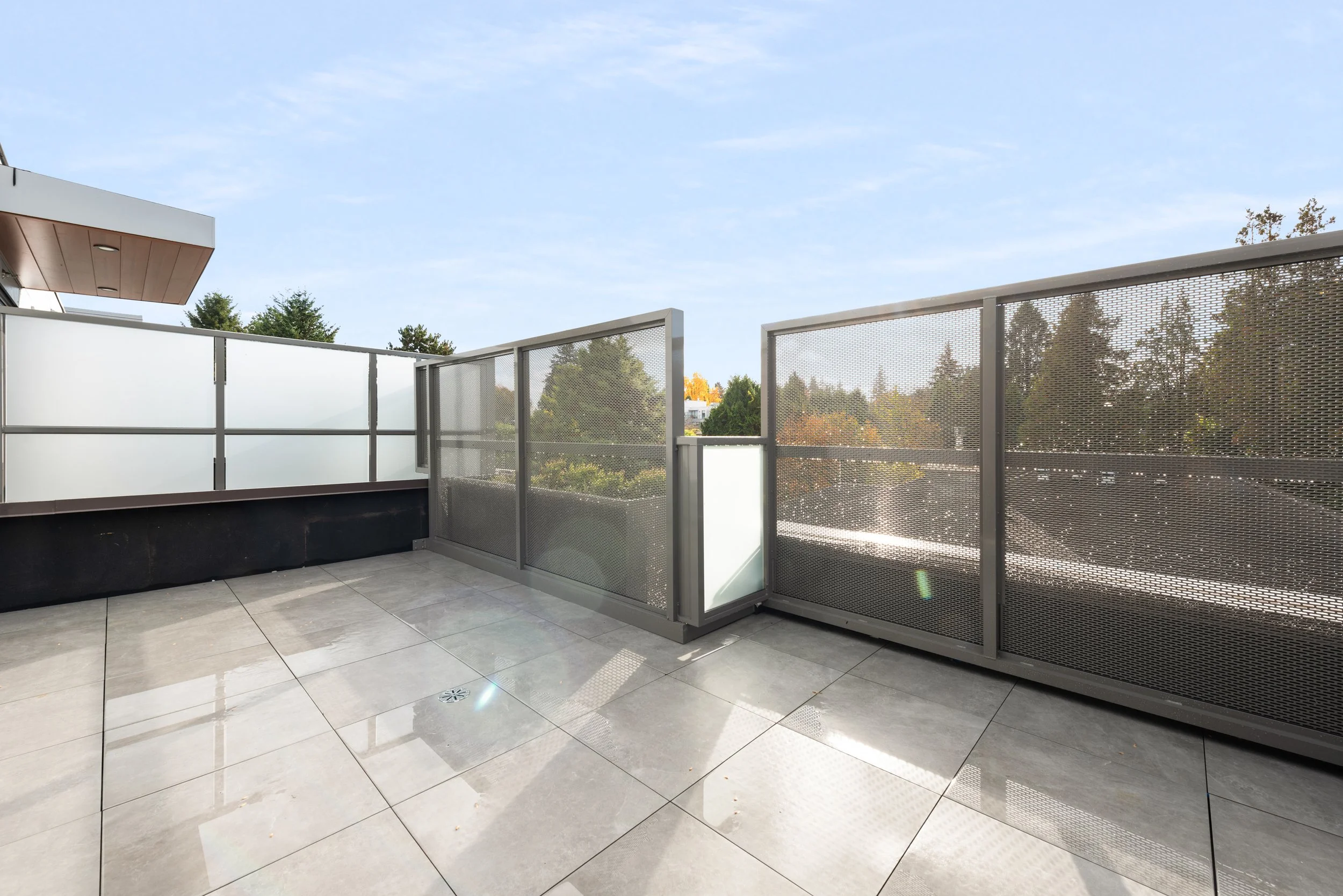 Empty balcony with glass and metal railings, overlooking trees and clear sky.