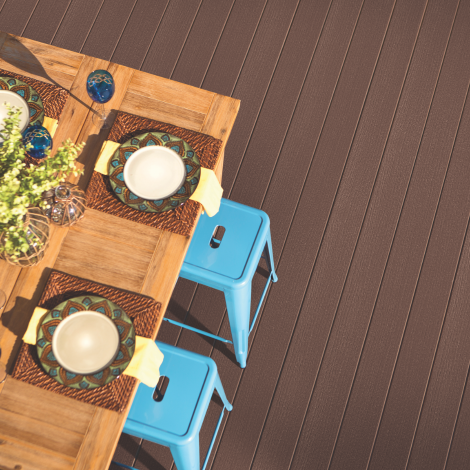 An outdoor dining setup with a wooden table, four place settings with patterned plates and napkins, and blue metal chairs on a wooden deck.