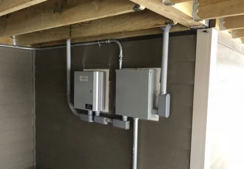 Electrical and utility boxes mounted on a concrete wall beneath a wooden structure.