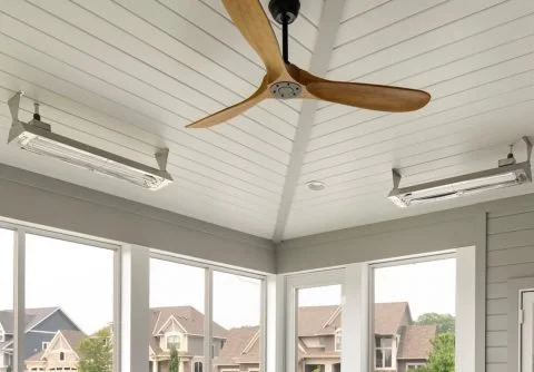 Ceiling with a wooden fan and two rectangular ceiling lights in a bright room with large windows showing houses outside.