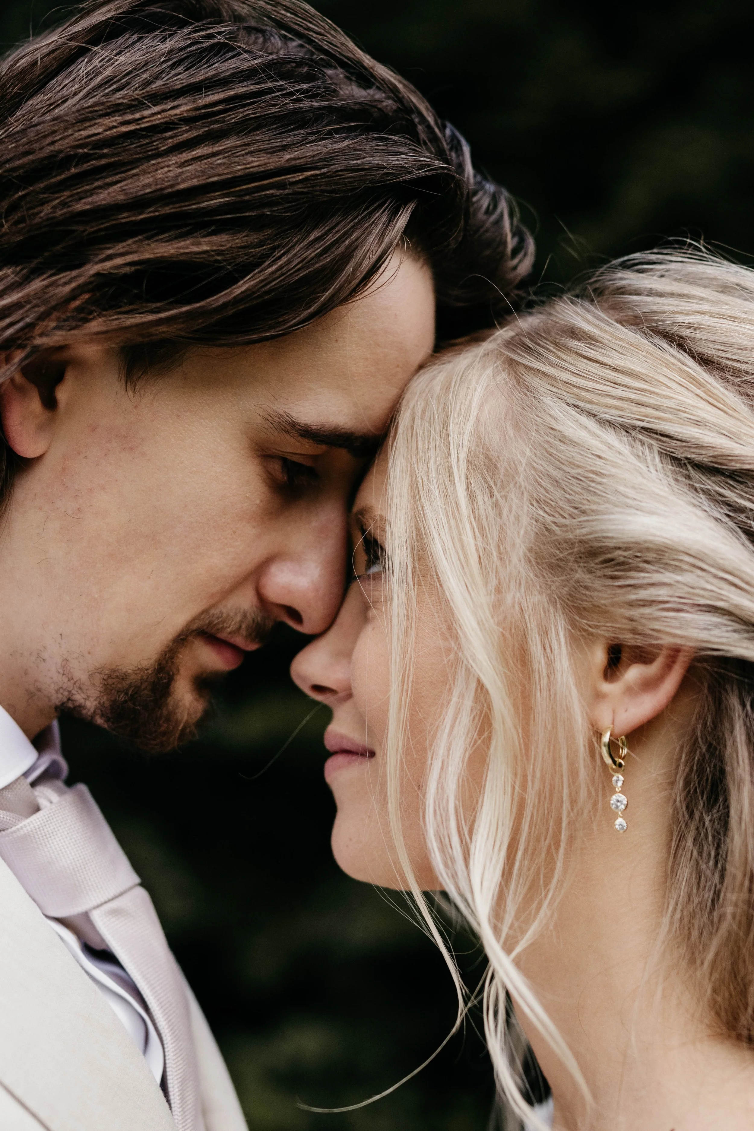 A close-up of a couple with their foreheads and noses touching, eyes closed, sharing an intimate moment outdoors.