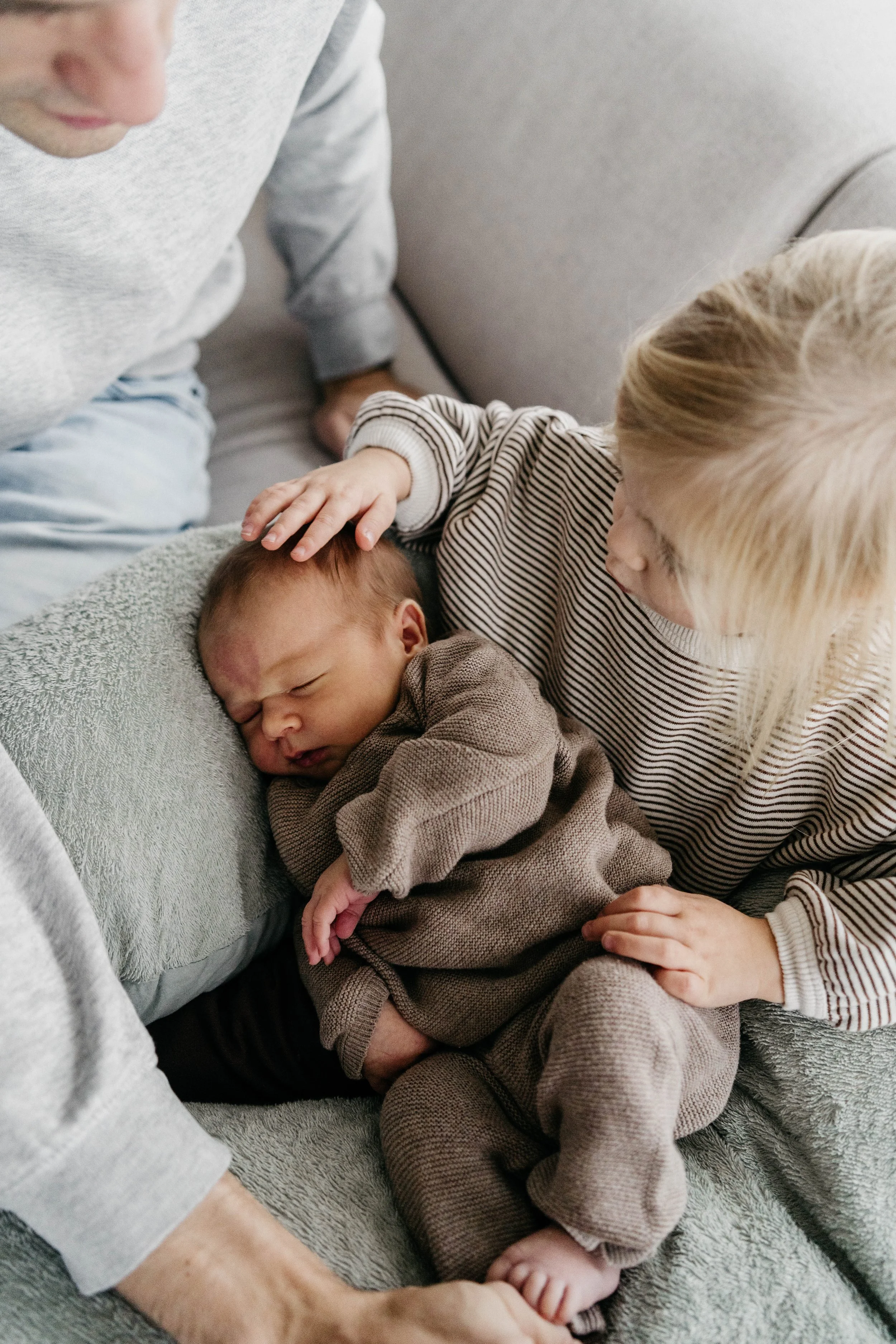 Young child gently touching a sleeping newborn on a cozy sofa.
