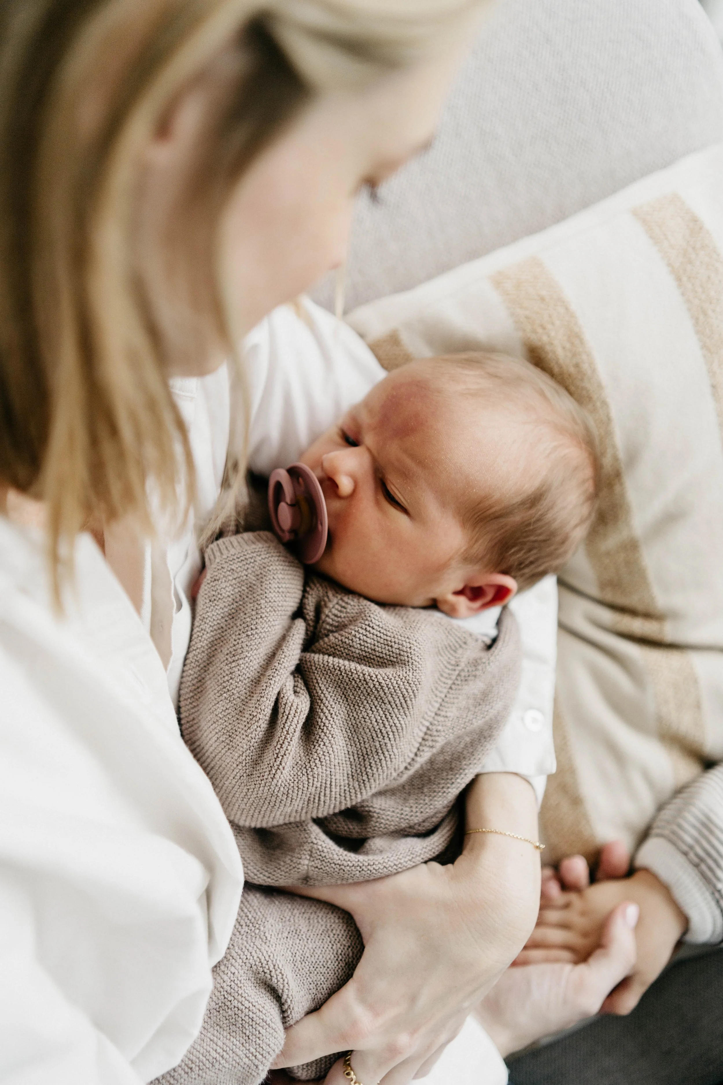 A woman holding a baby who is breastfeeding, lying on her chest on a beige couch.