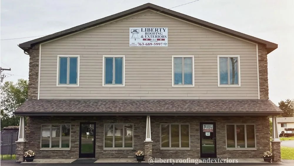 Two-story building with a stone and beige siding exterior, windows, and a sign for Liberty Roofing & Exteriors LLC on the upper level.