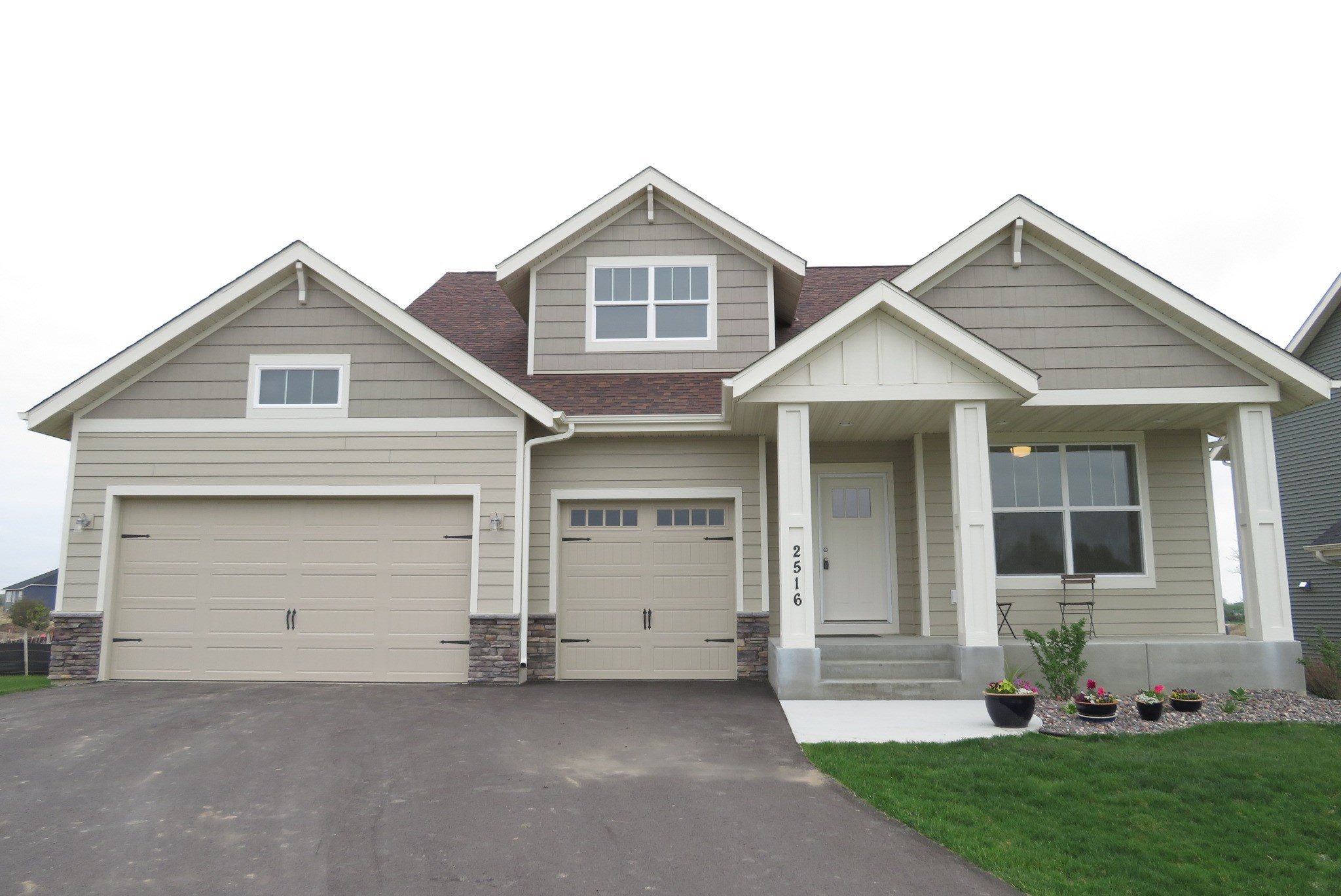 Front view of a modern two-story house with a beige exterior, covered porch, and a driveway leading to a two-car garage.