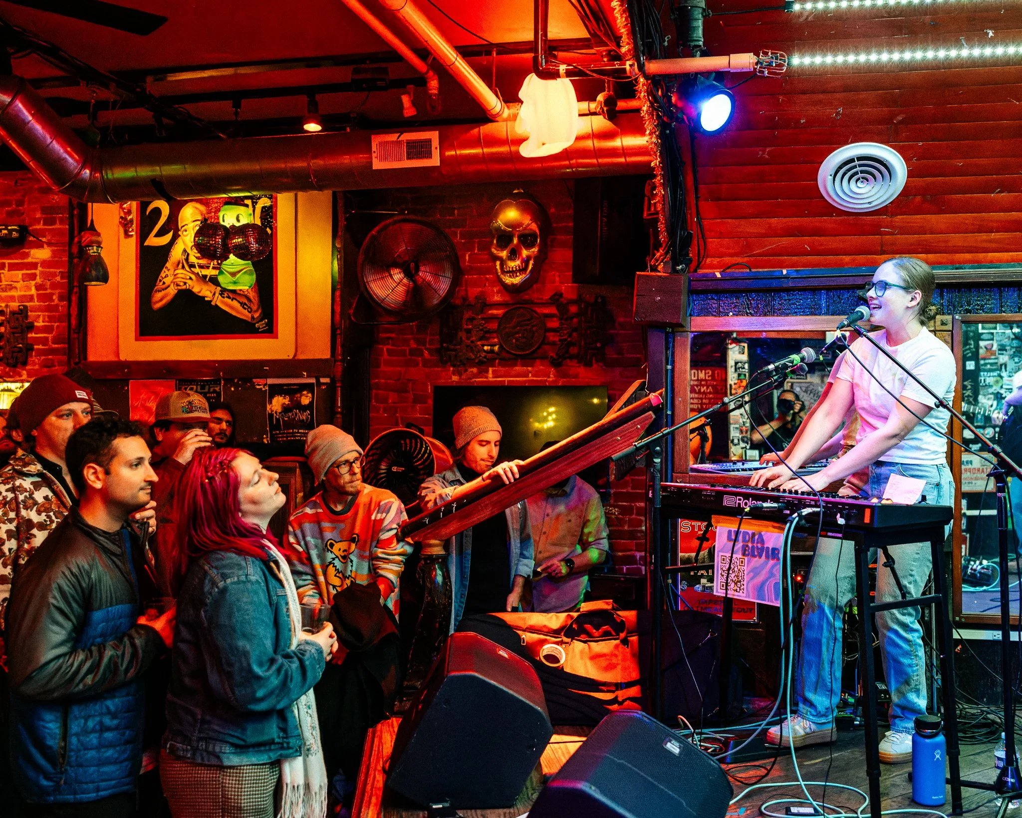 A woman performing on stage with a keyboard, singing into multiple microphones, while a captivated audience listens and dances along.