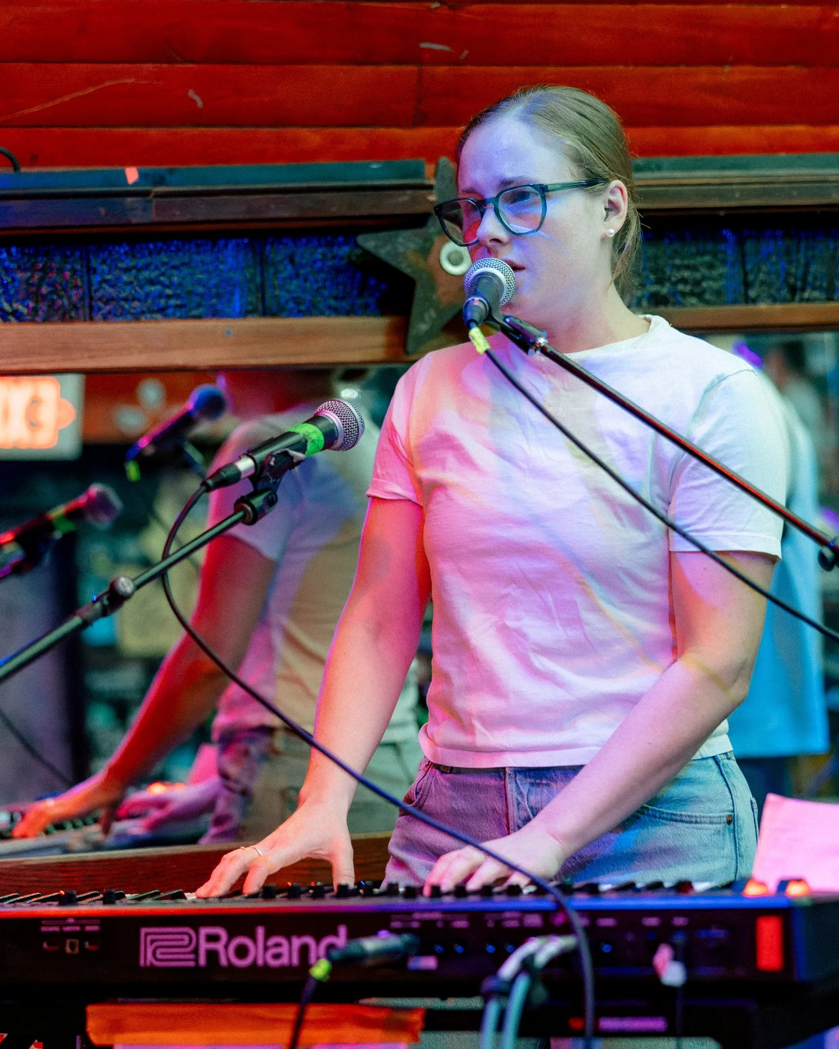 A performer singing into a microphone and playing a Roland keyboard in a bar or music venue.