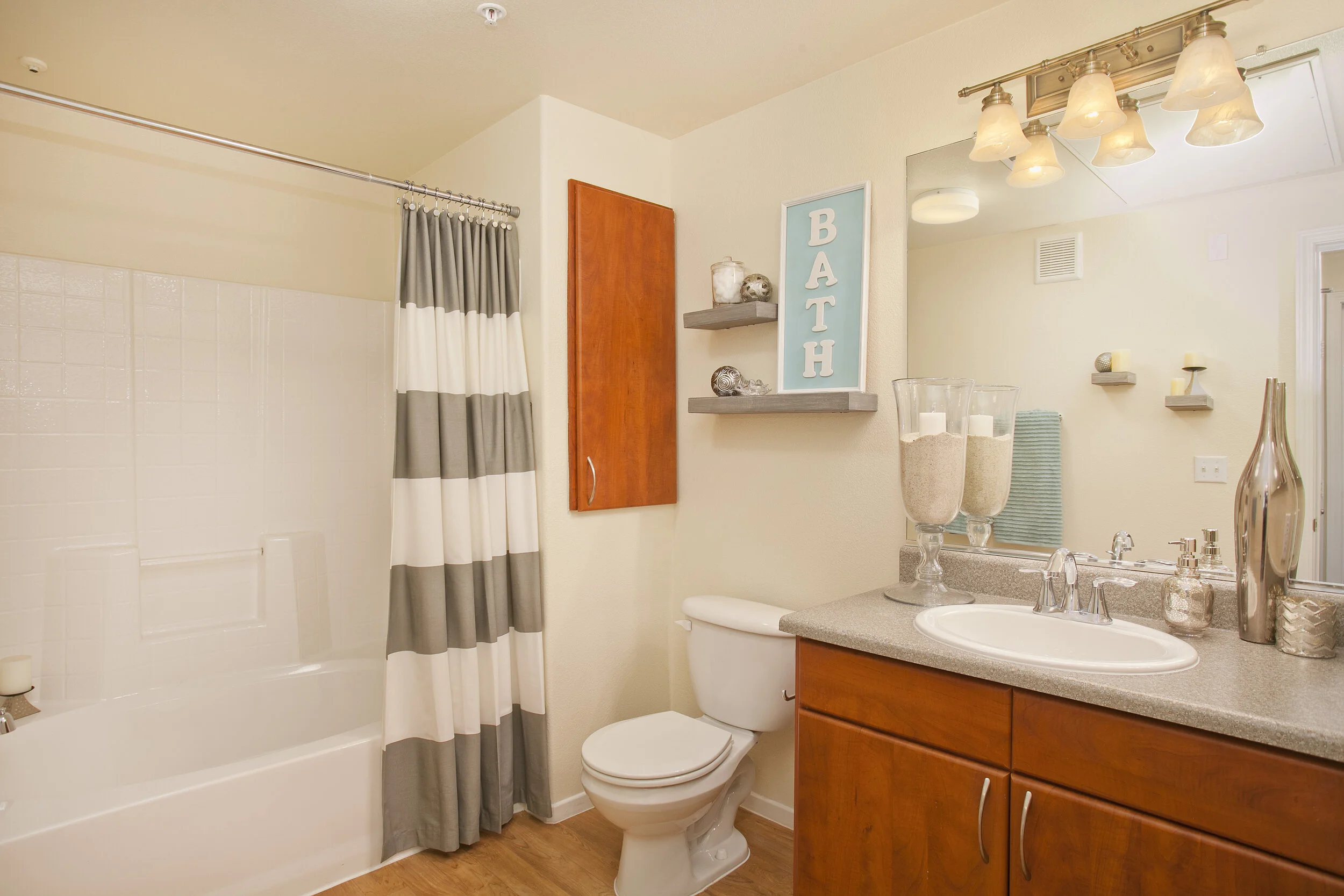 Bathroom at The Overlook at Rancho Belago with wood plank flooring, brown wood cabinets, large mirror, and a shower/tub. 