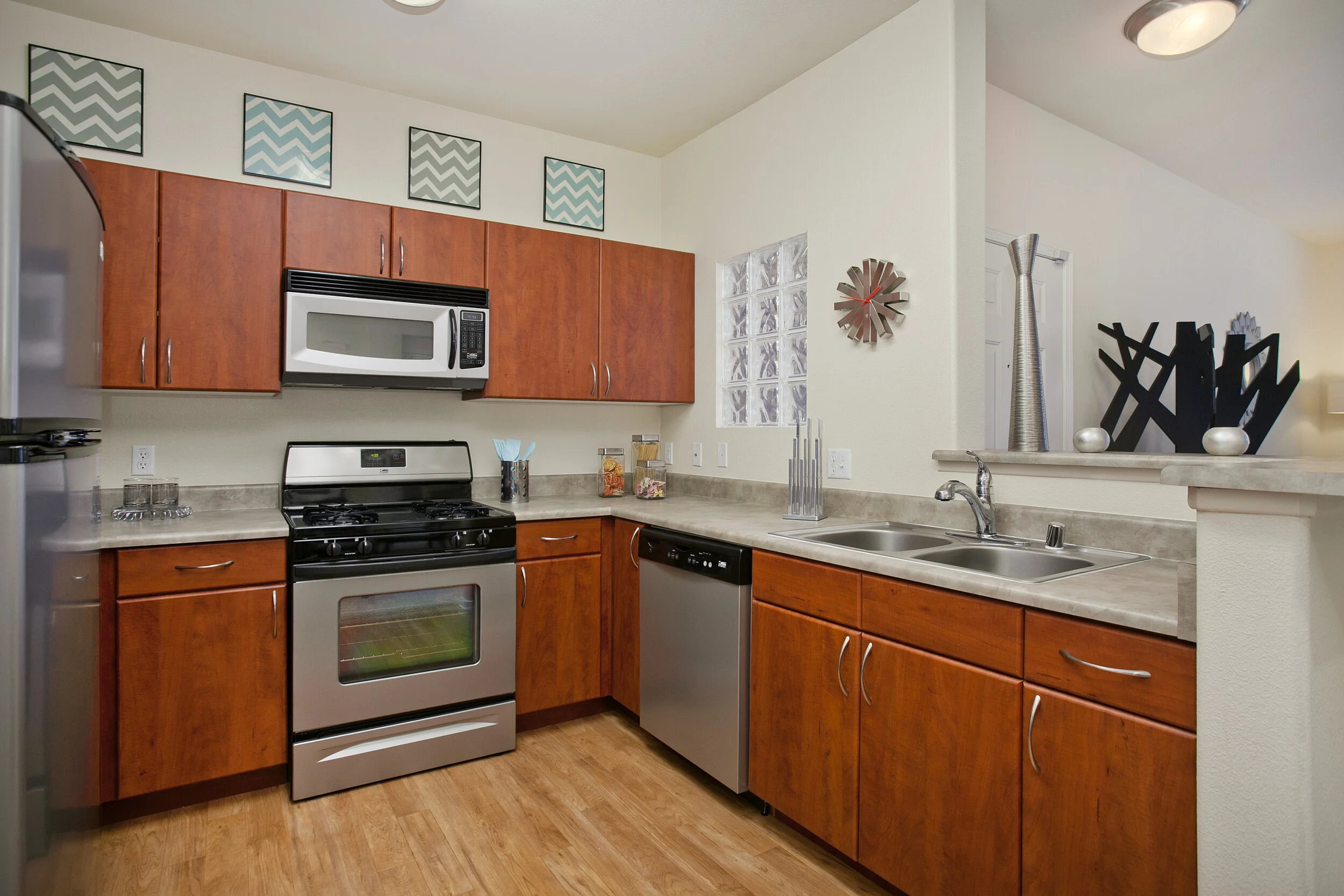 Kitchen inside unit at The Overlook at Rancho Belago with brown cabinets, stainless steel appliances, wood plank flooring, and cream walls. 