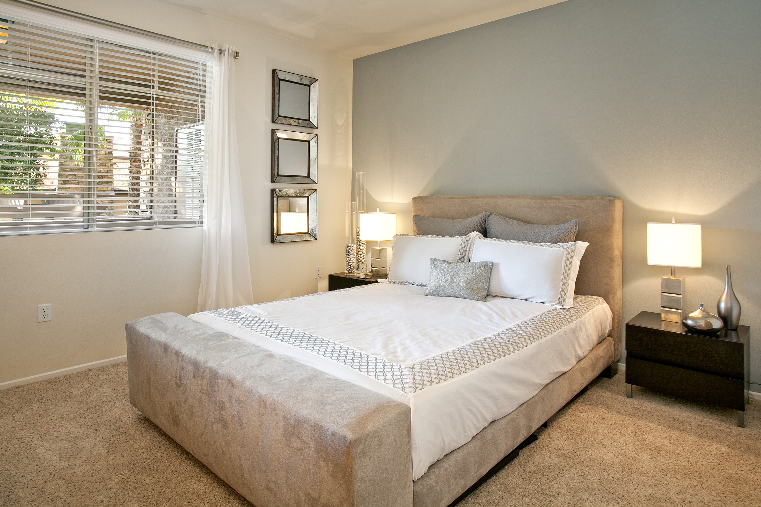 Bedroom inside apartment at The Overlook at Rancho Belago with carpeted flooring, cream walls, one blueish grey accent wall, and large window. 