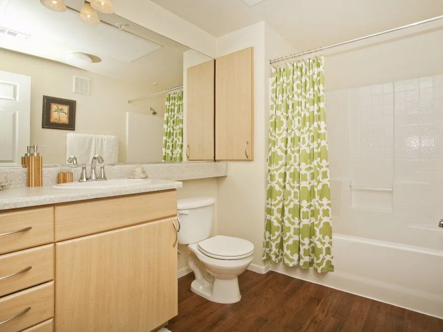 Bathroom in apartment at The Overlook at Rancho Belago with light wood cabinets, wood plank flooring, a shower/tub, and a large mirror.
