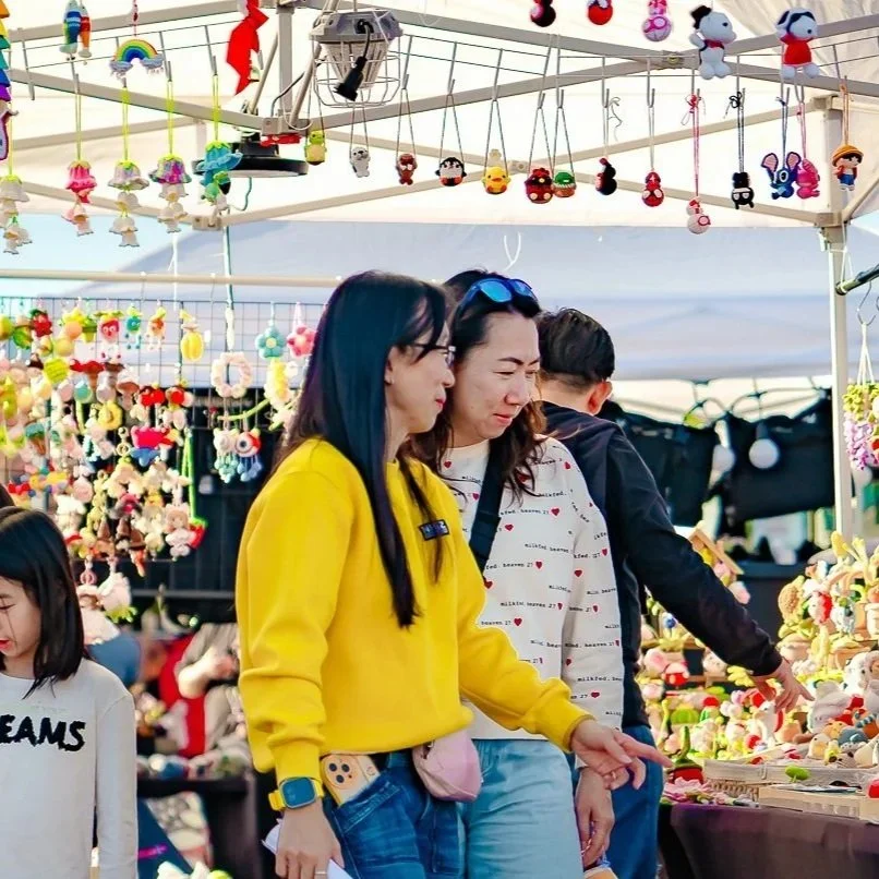People shopping for colorful plush toys and crafts at an outdoor market stall.