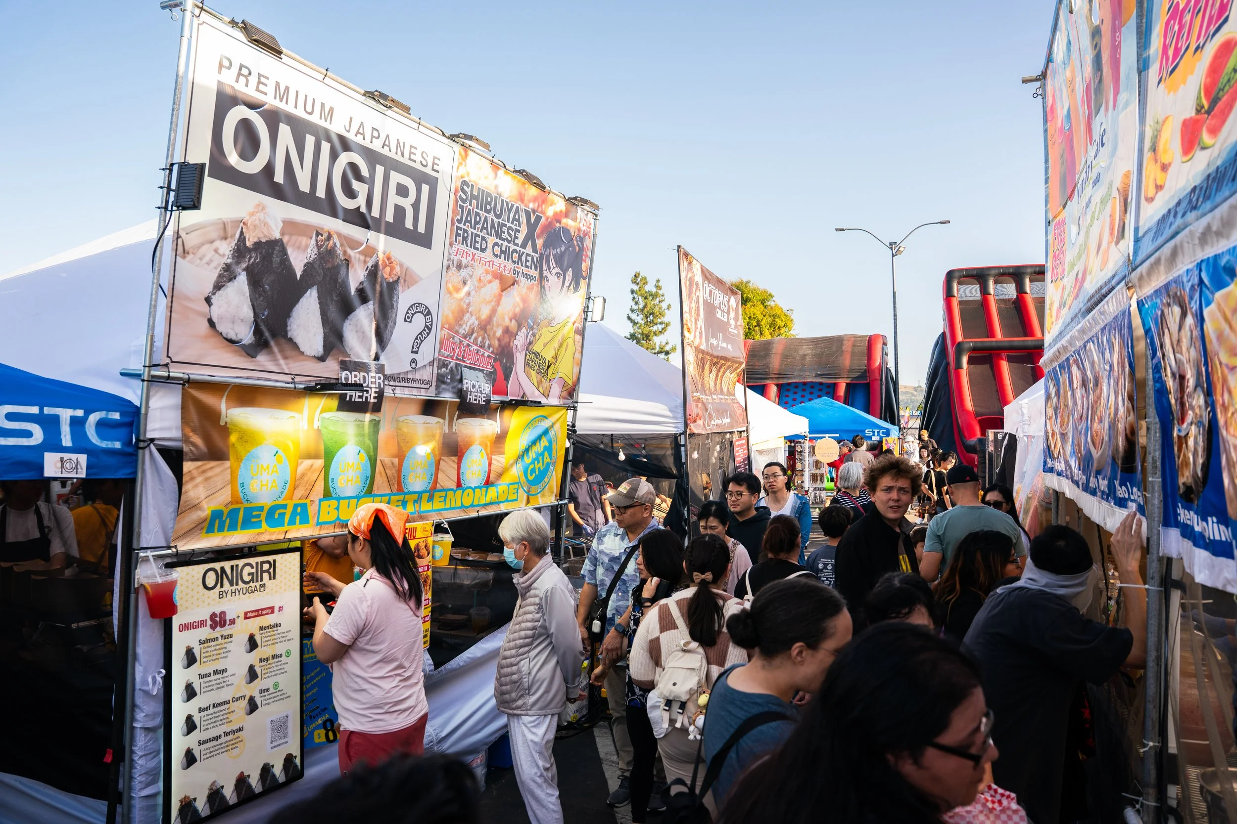 A large crowd of people at the OCAL Natsu Festival, a Japanese inspired night market festival at STC Rowland Legacy. There are multiple Japanese and global food vendors and lines of people waiting to get food. The background shows a large inflatable 