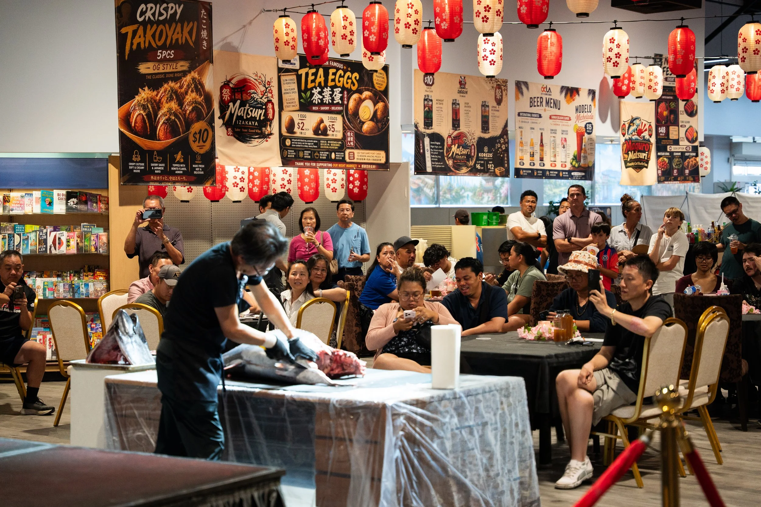 A crowd sitting in the izakaya eating area of the Legacy Pavilion is watching the sushi master demonstrate and explain the process of using the whole bluefin tuna. The sashimi will be processed and freshly prepared for the audience to try. 