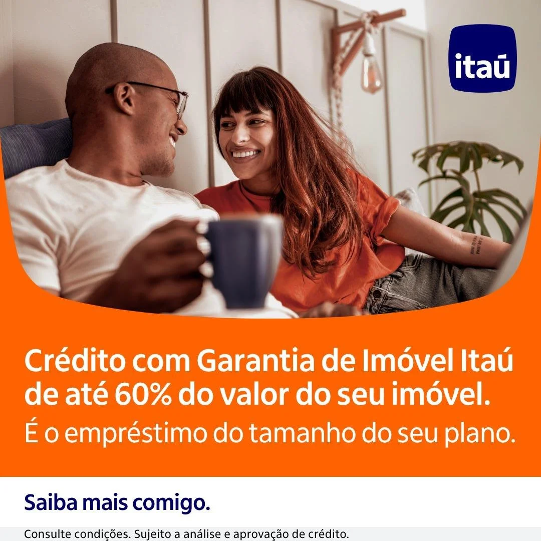 Imagem de um casal sorridente sentado no sofá, com um copo na mão, promovendo um crédito com garantia de imóvel do Itaú de até 60% do valor do imóvel.