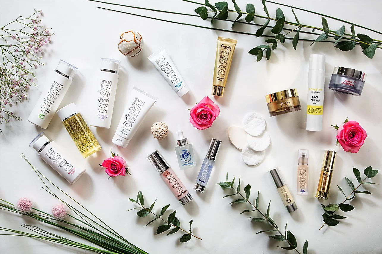 Verschiedene Hautpflegeprodukte und Kosmetika liegen auf einem weißen Hintergrund, umgeben von Blumen und grünen Zweigen.