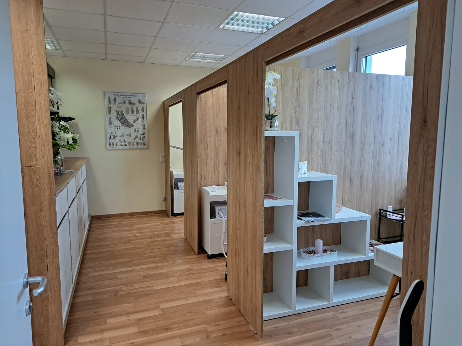 Büro- oder Behandlungsraum mit Holzabtrennungen, weißen Schränken und Dekorationen wie Blumen und Kerzen.