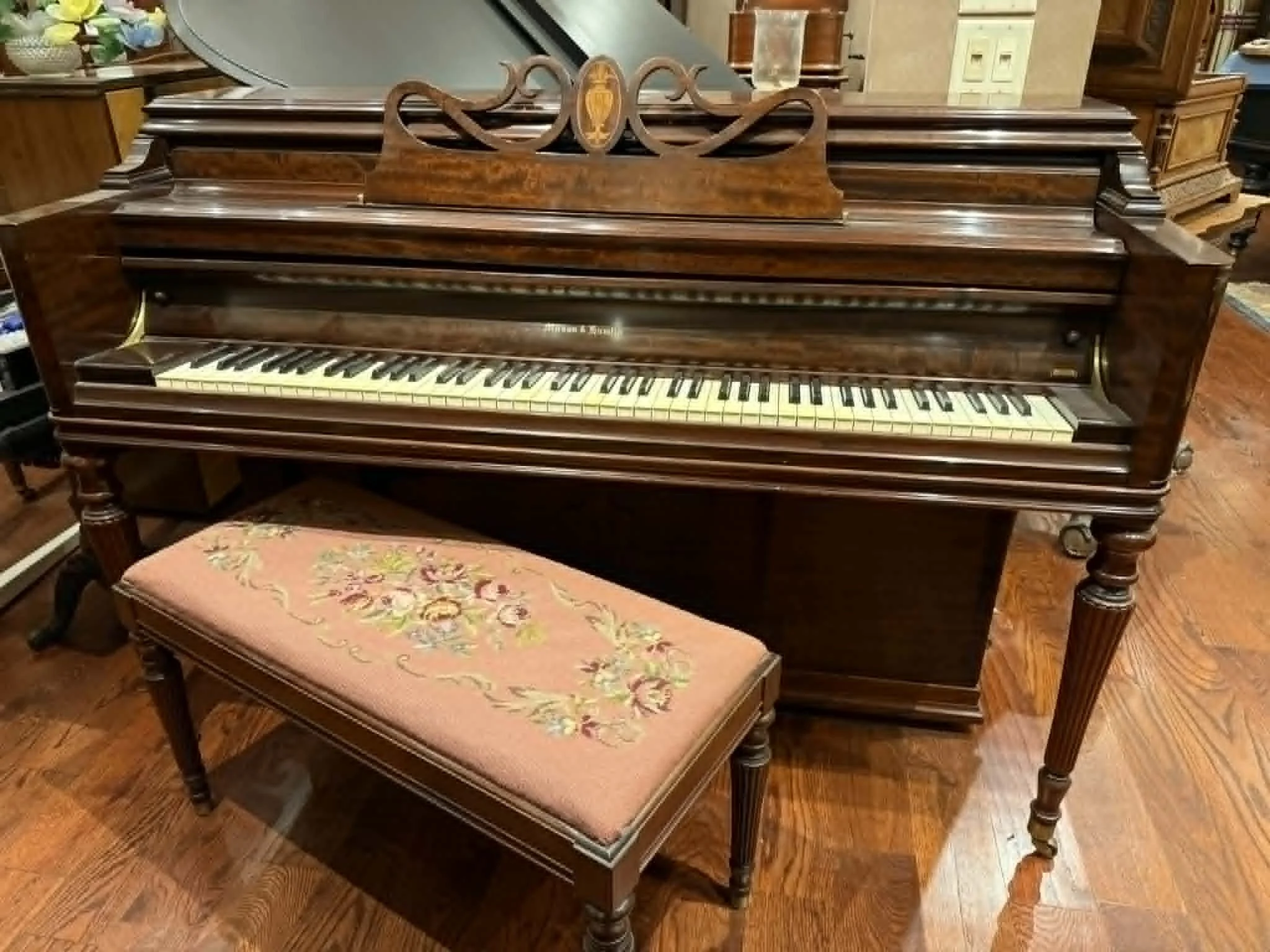 A vintage wooden upright piano with a matching stool in a room with wooden floors and furniture.