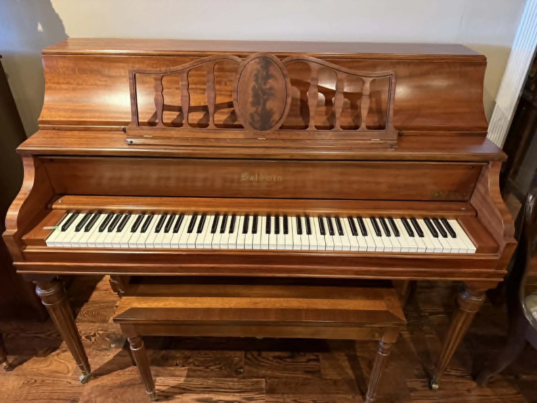 A vintage upright wooden piano with a matching bench, featuring a carved music stand and black and white keys.