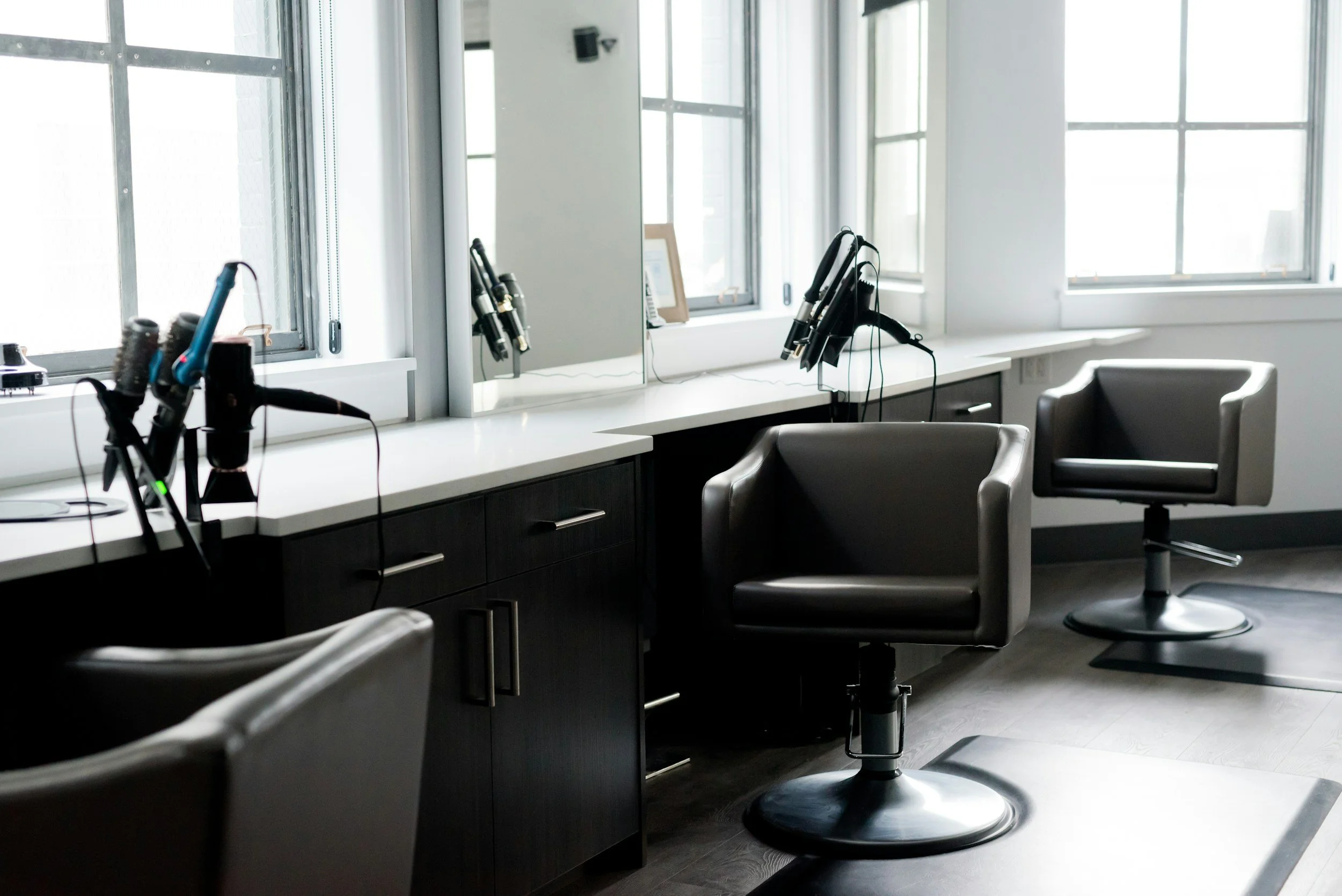 Salon with black chairs, hair styling tools, and a large mirror near windows in a modern salon.