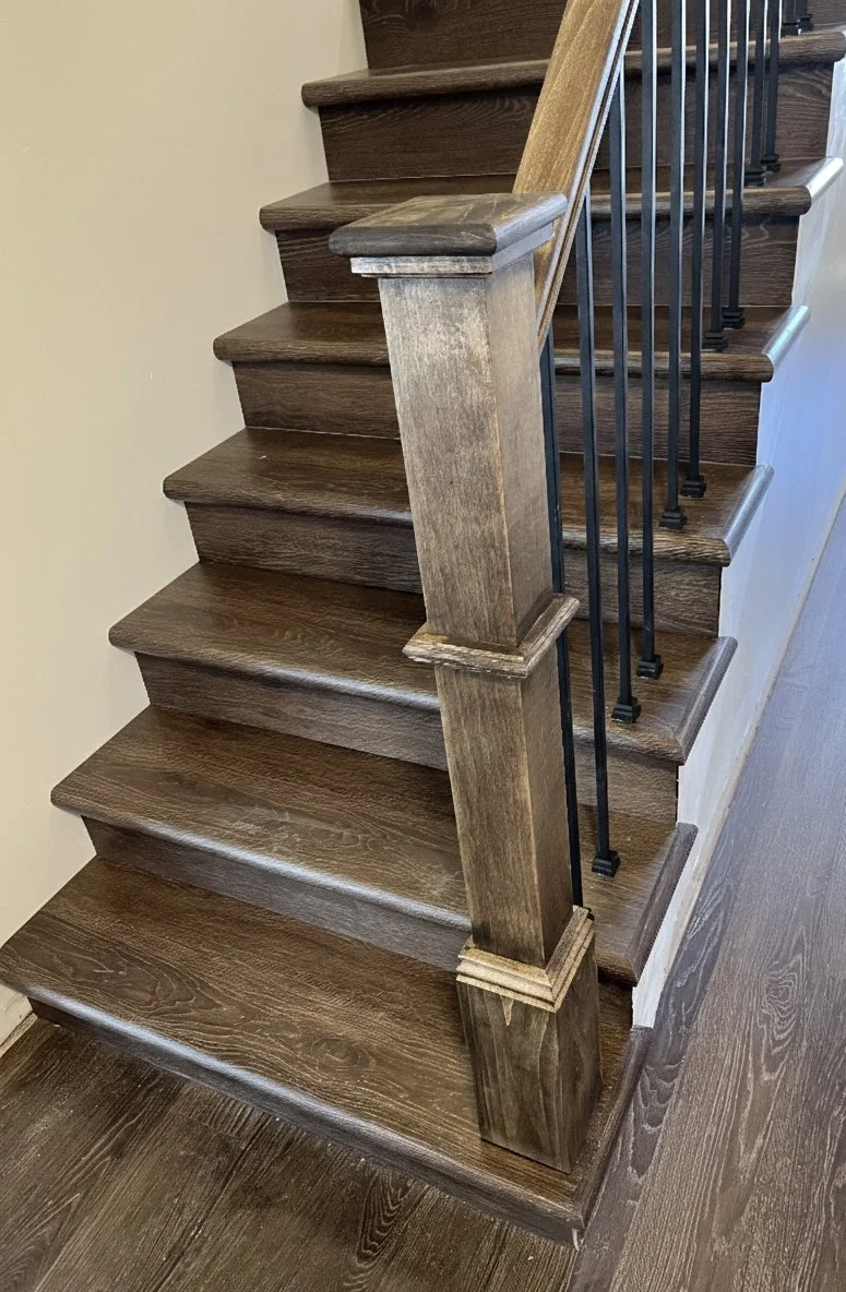 Close-up of a staircase with dark wooden steps, a wooden handrail, and black metal balusters.