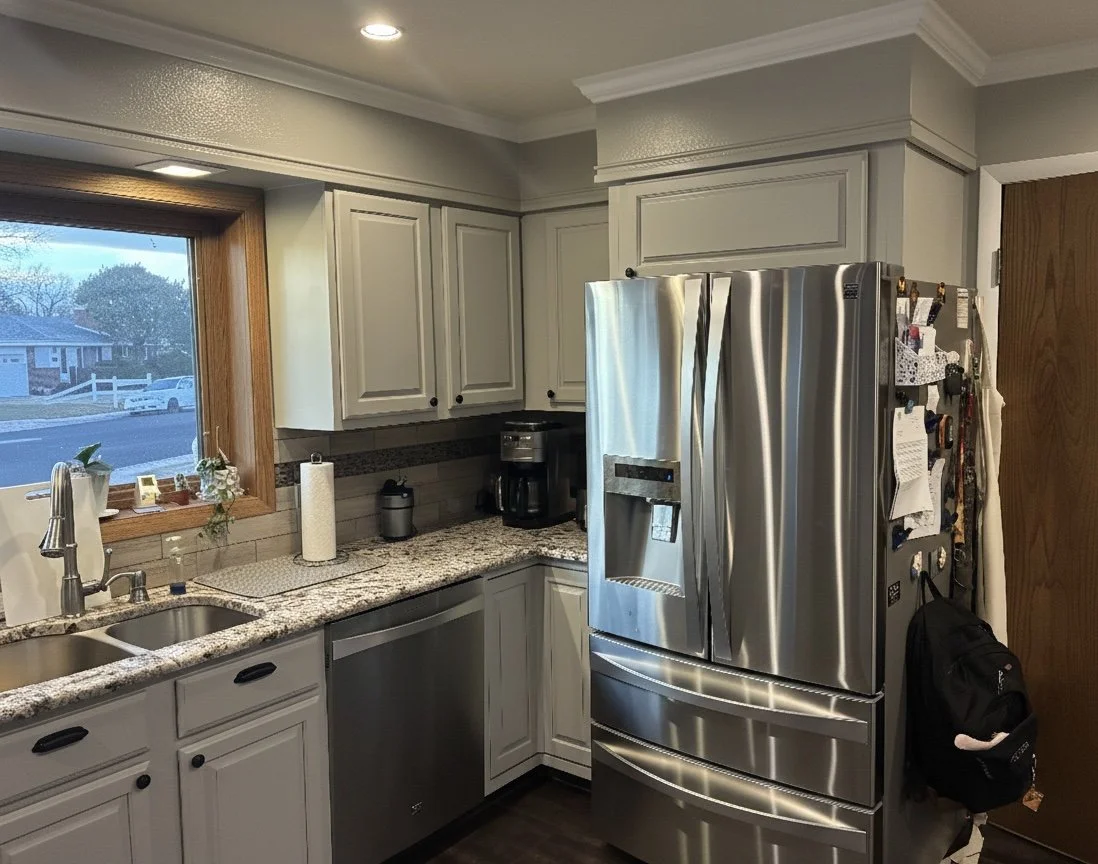 Kitchen with granite countertops, white cabinets, stainless steel refrigerator, and a window showing a suburban street outside.