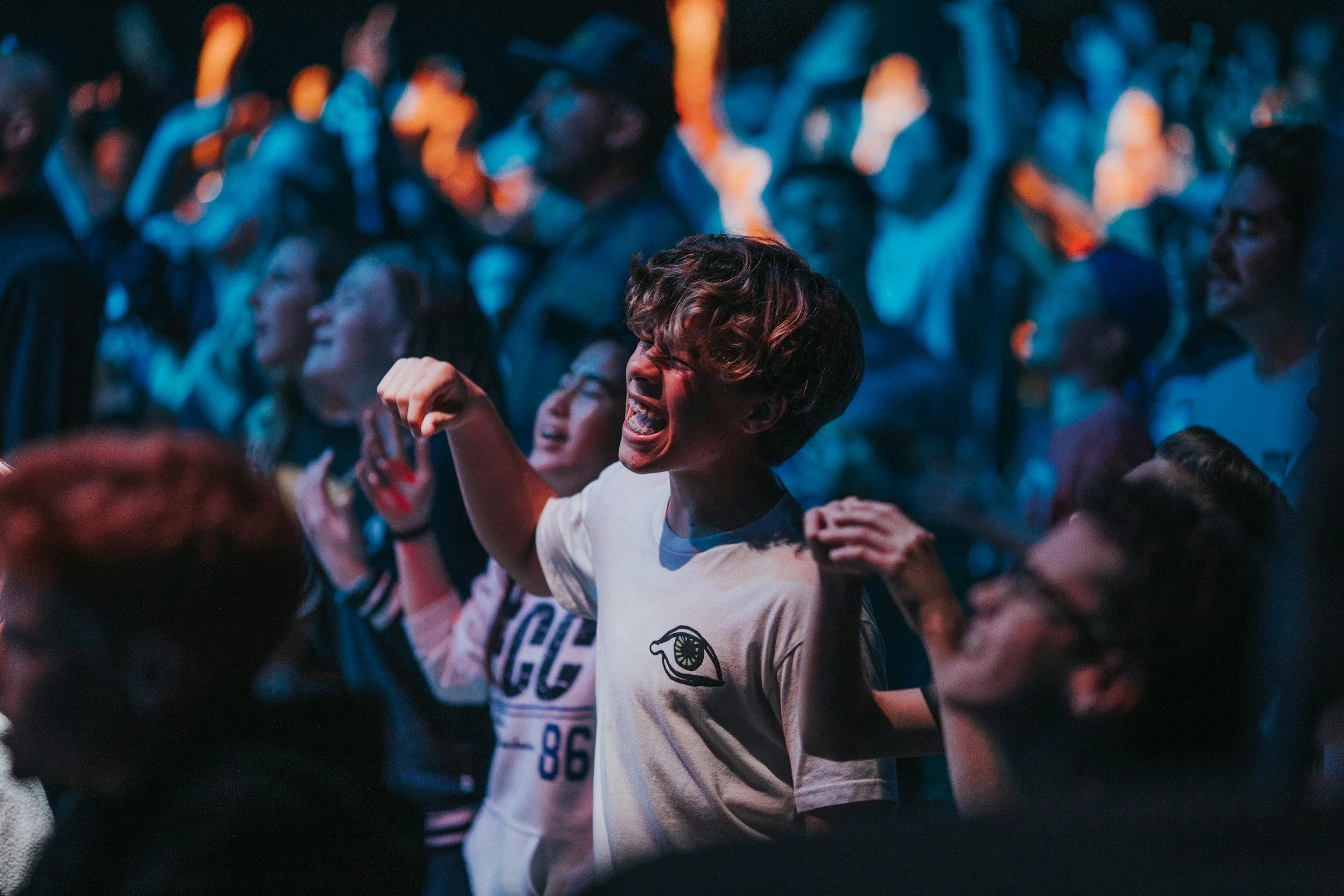 Crowd of people at a concert or event, some cheering and dancing, with a woman in the foreground expressing excitement and joy.