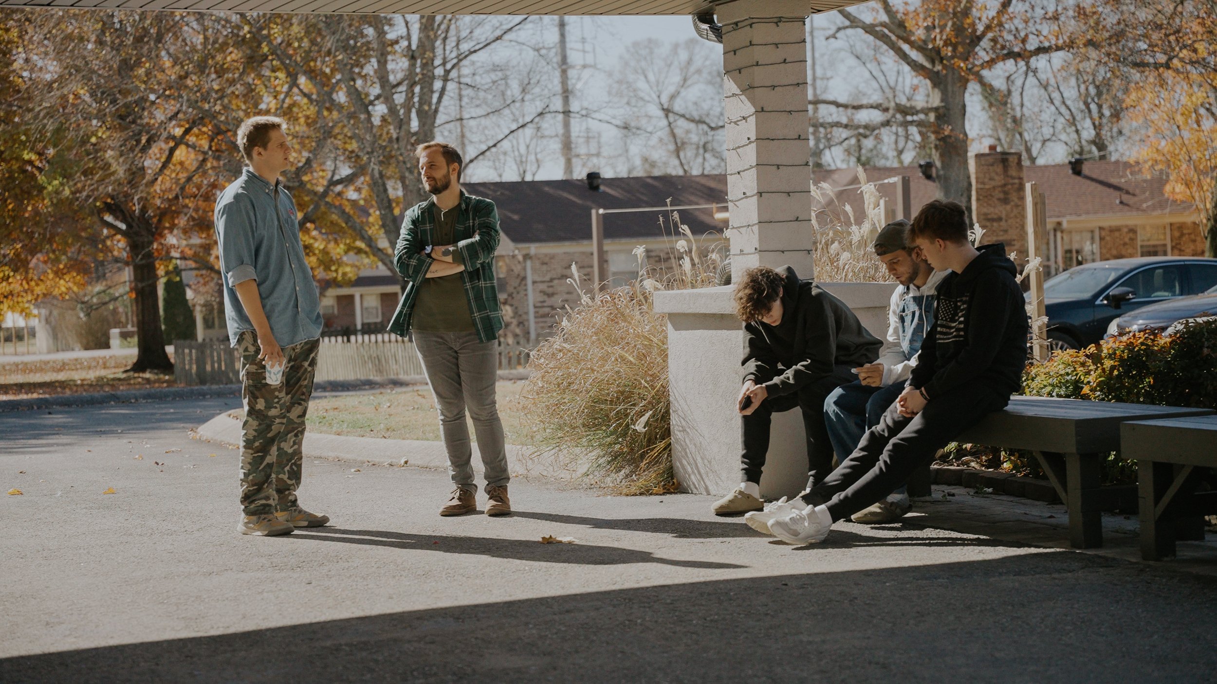 Group of young people sitting and standing outside of Vineyard Church Franklin on a sunny autumn day with trees and houses in the background.