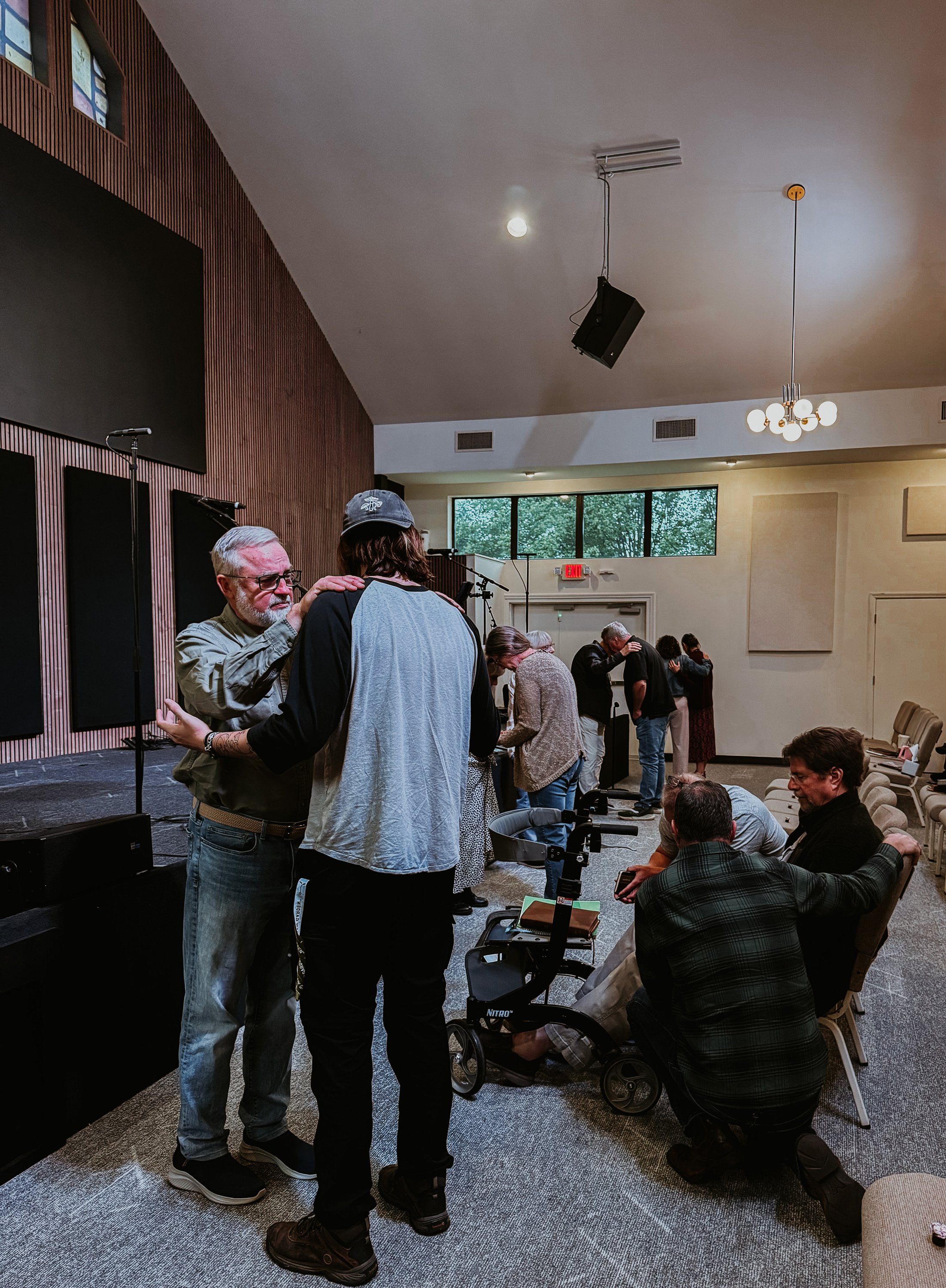 People praying and comforting each other inside a church or event hall.