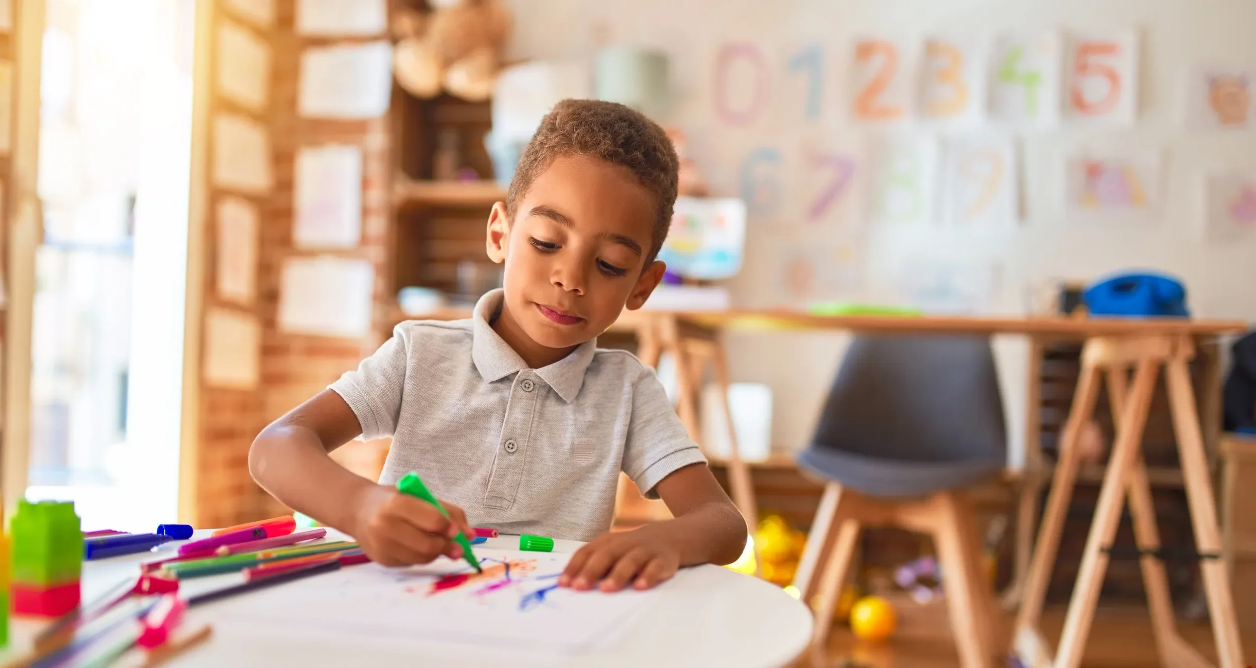 A boy at a white table coloring with markers