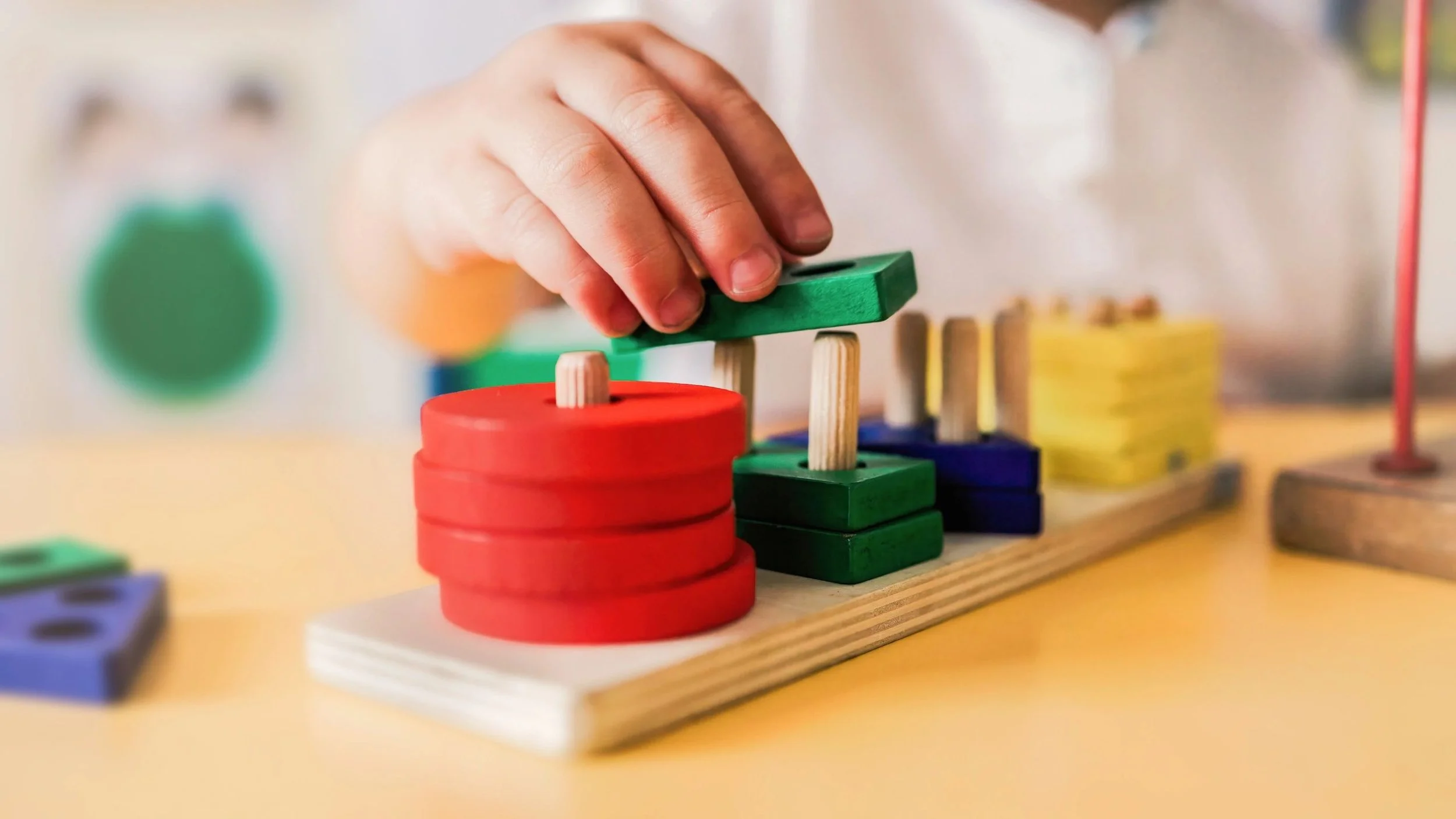 A hand of a child with green and red blocks being placed on a wood stand