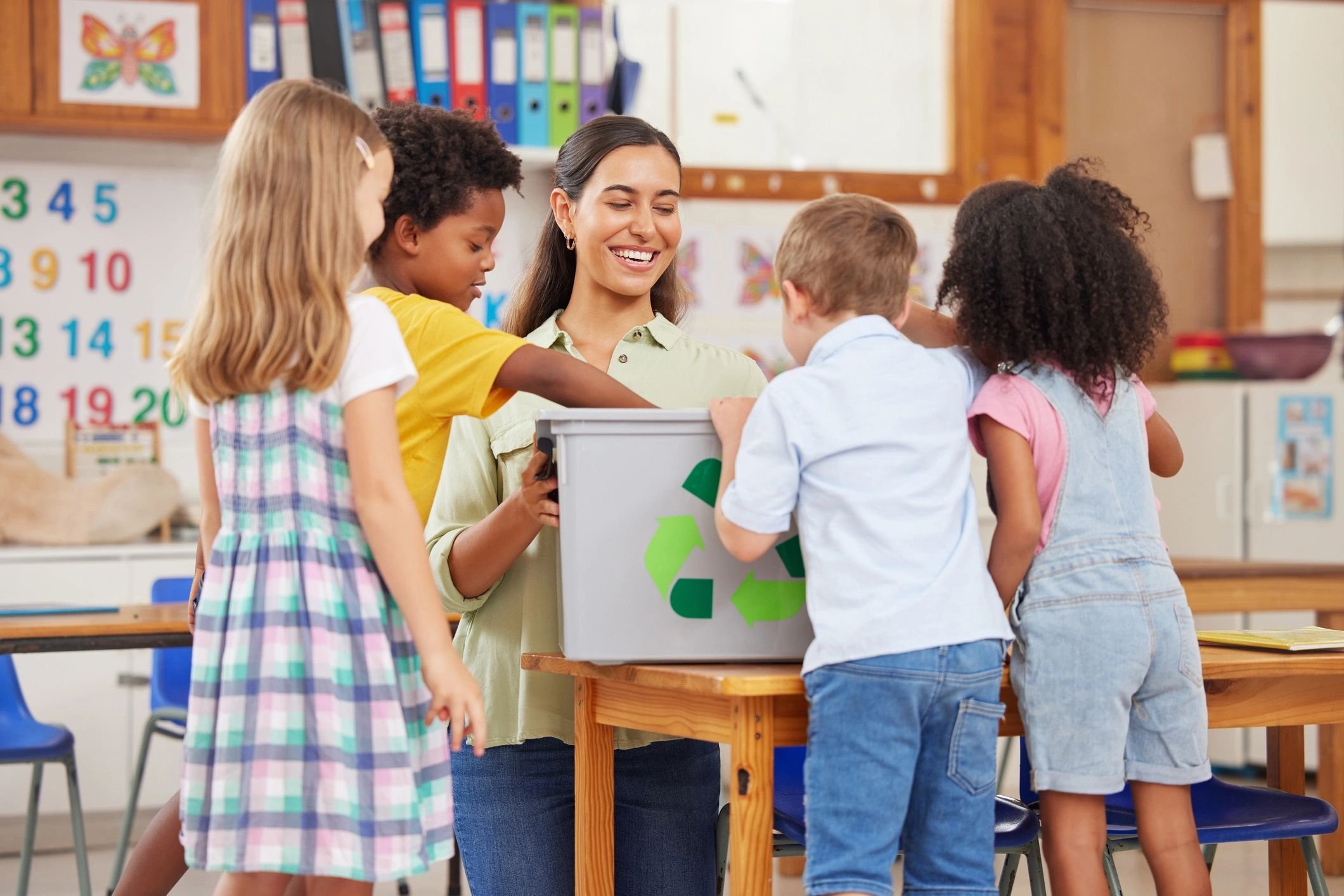 A teacher with four children smiling, standing around a gray box