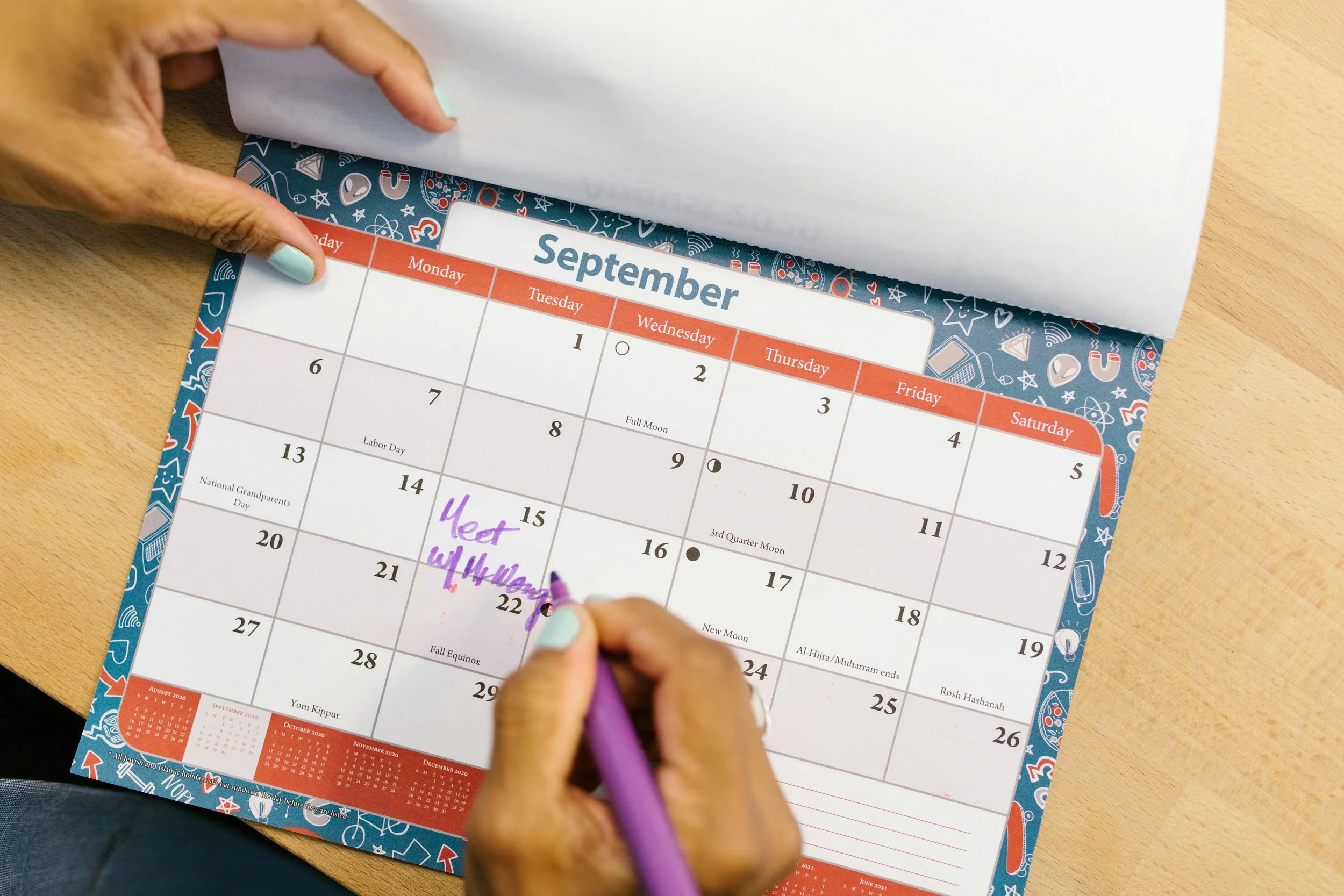 Person marking a calendar for September with a purple marker, writing 'Meet W' on the 15th, with other notes and dates visible.