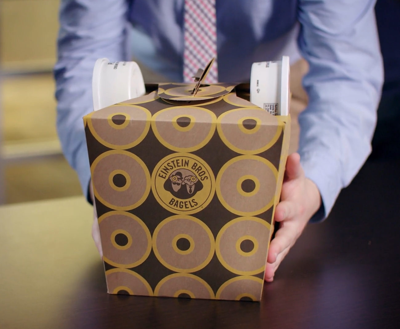 Person holding a takeout box from Einstein Bros Bagels with a bagel, cream cheese, and butter inside.